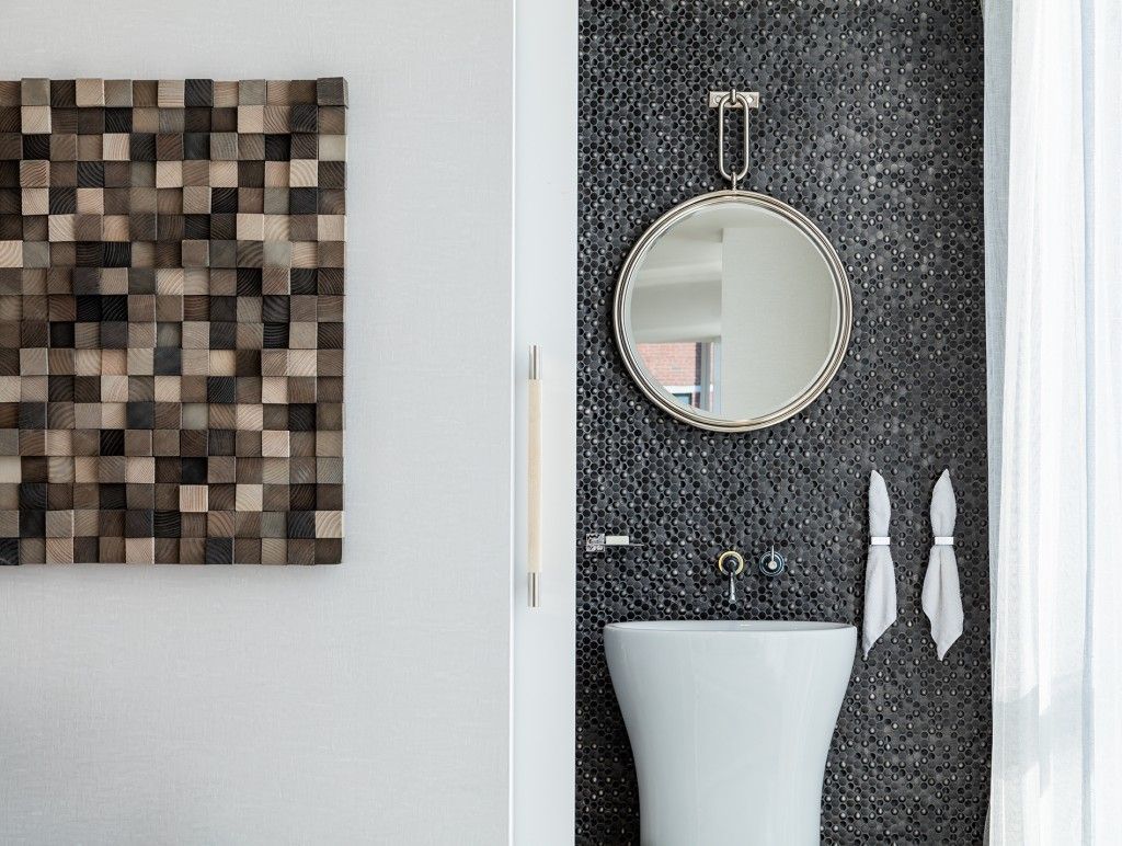 Modern bathroom with mosaic wall, round mirror, white sink, wooden art.