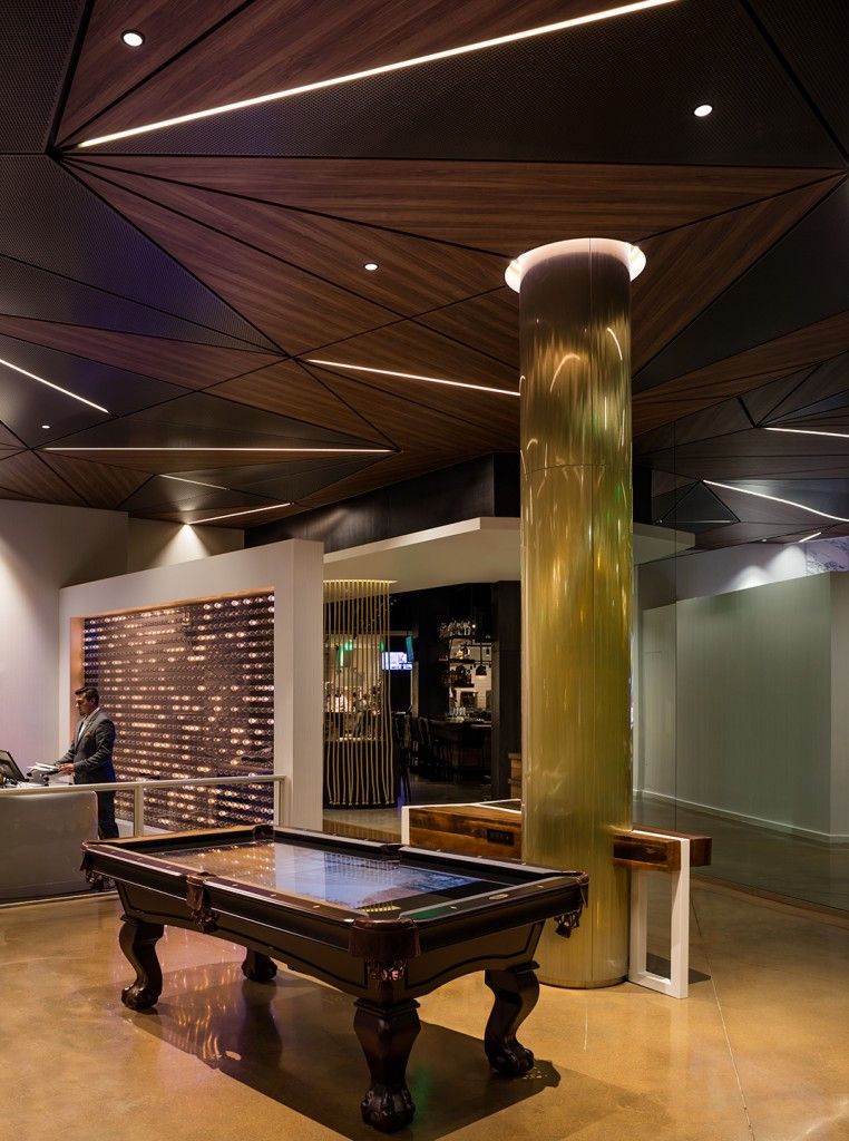 Pool table in a modern room with a decorative ceiling, a large gold column, and a person at the front desk.