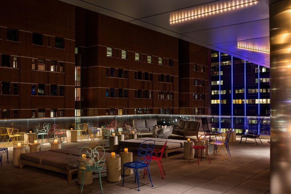 Rooftop lounge at night with modern furniture, city backdrop, candles, and colorful chairs.
