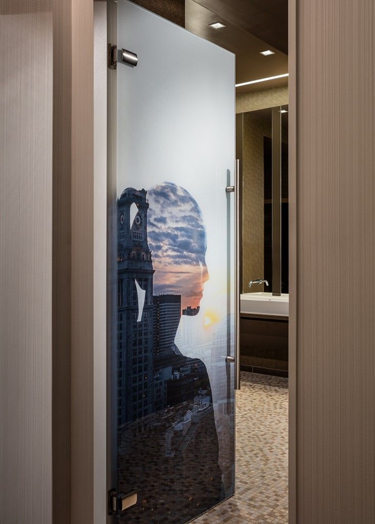 Frosted glass door with a cityscape overlay leading into a bathroom. The door has a handle and is open.
