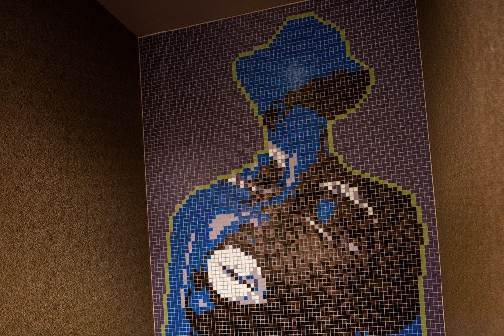 Blue silhouette art on a textured wall, possibly a figure wearing a hat.