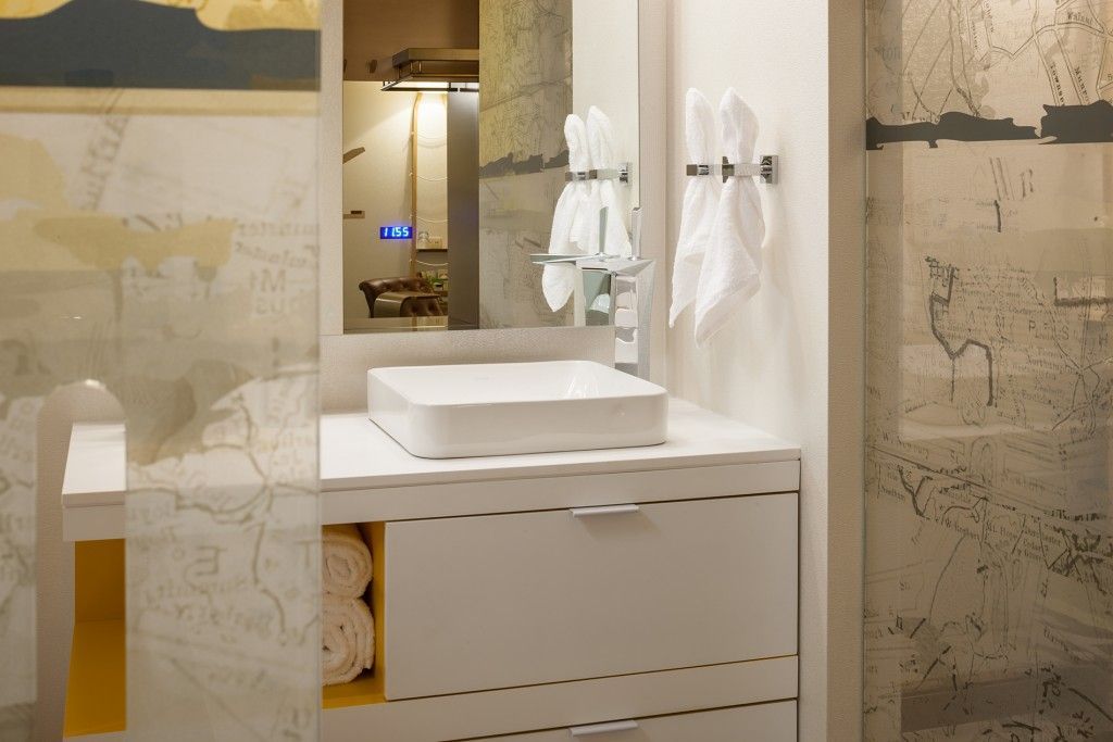 Modern bathroom with white sink, cabinet, and towels. Gold and grey accents, mirror.