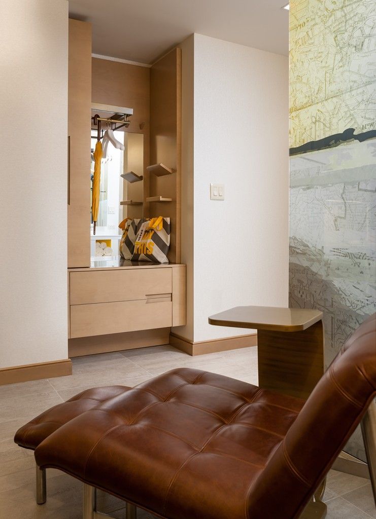 Brown leather chaise lounge by a closet, light wood shelves and cream walls.