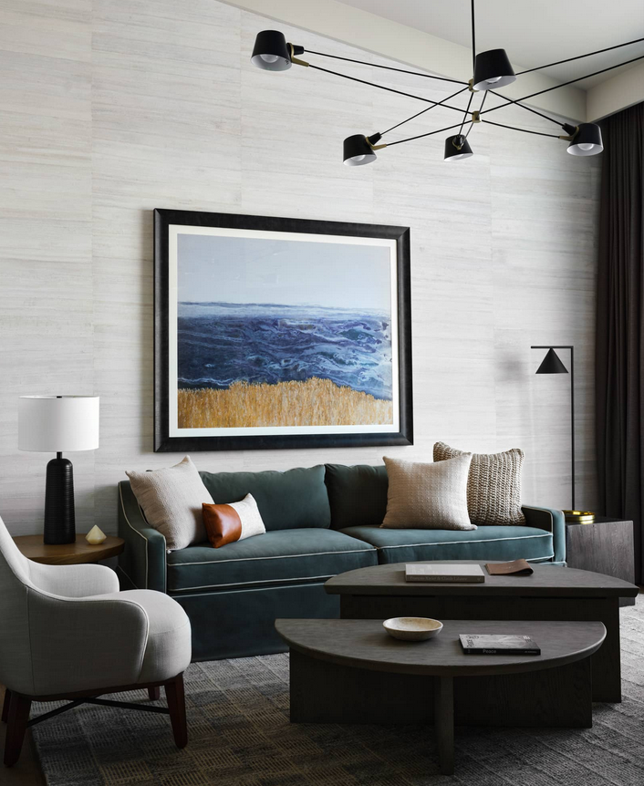 Living room with teal sofa, artwork of ocean, and modern lighting fixtures.