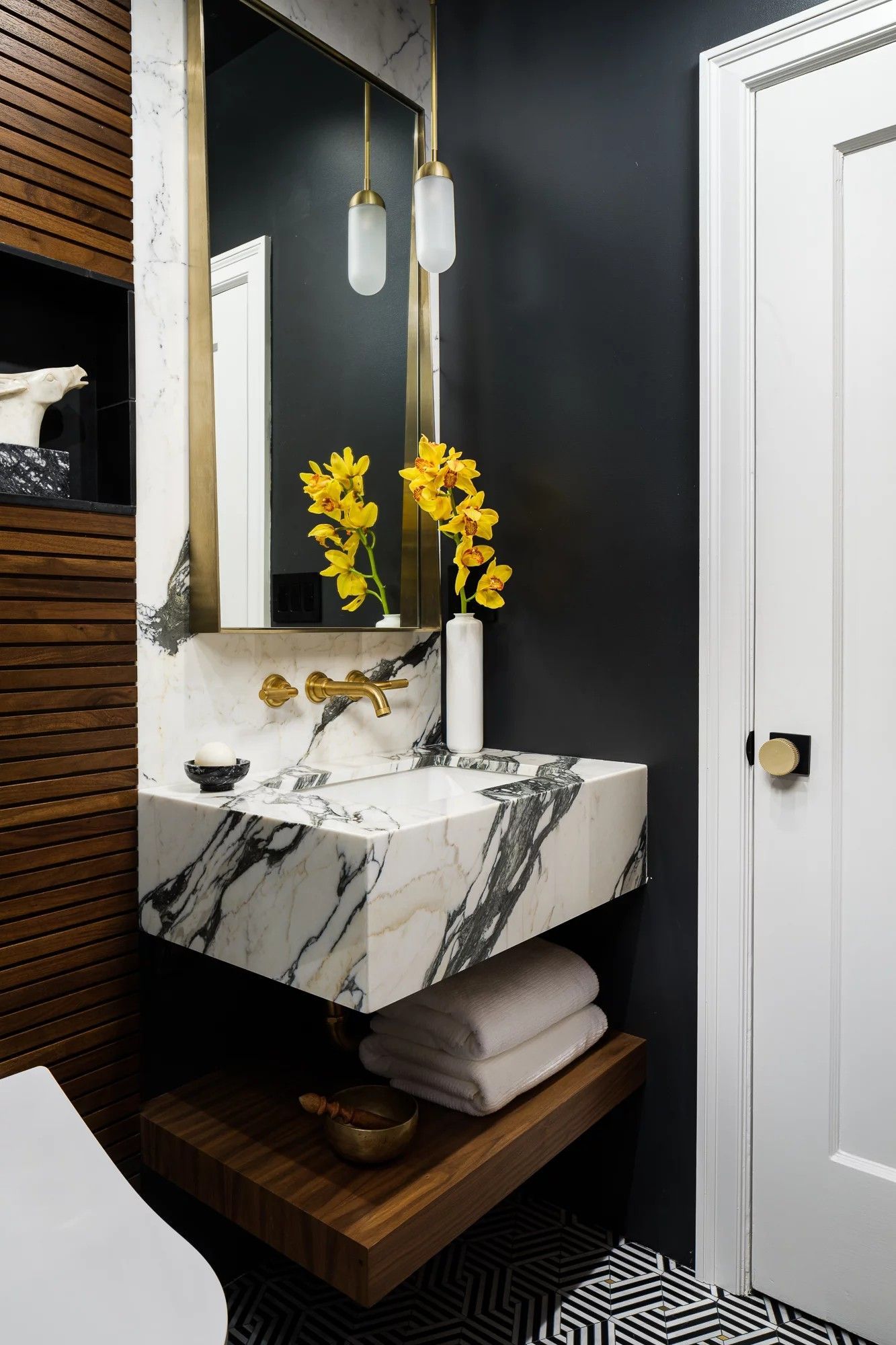 Modern bathroom with marble sink, gold fixtures, dark gray wall, and wood accents.