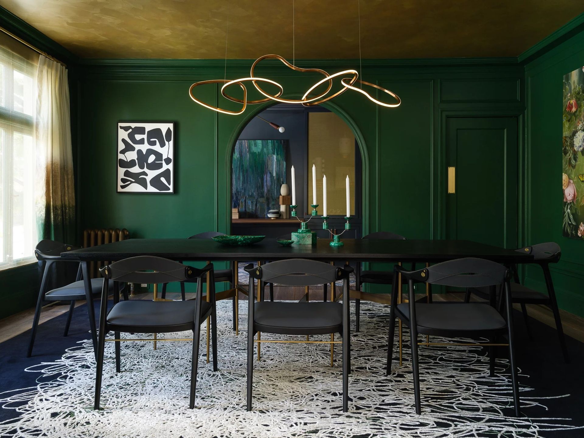 Emerald green dining room with black table and chairs, gold ceiling, arched doorway, abstract art, and modern chandelier.
