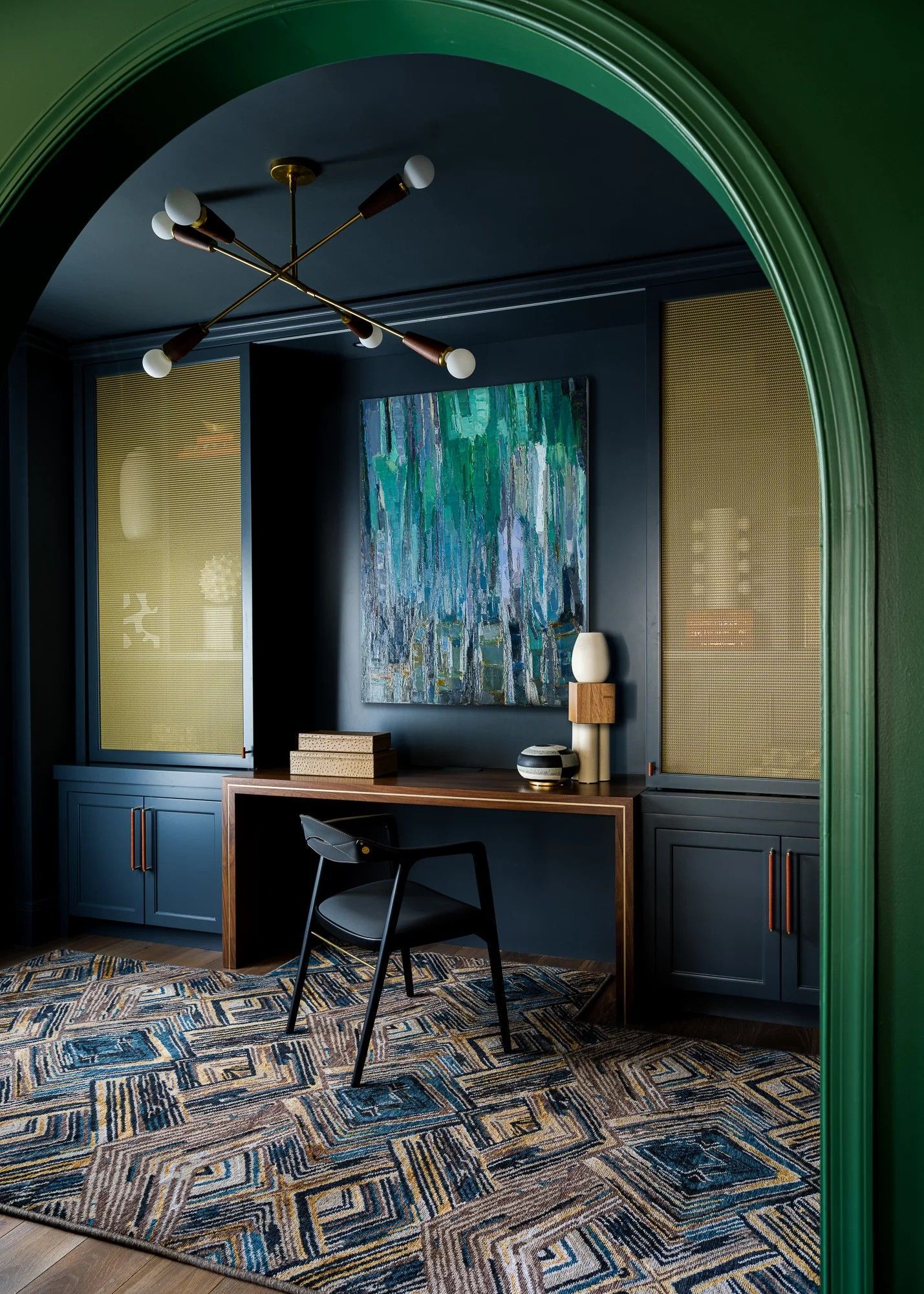 Dark blue office with gold accents and an abstract painting, viewed through a green archway.
