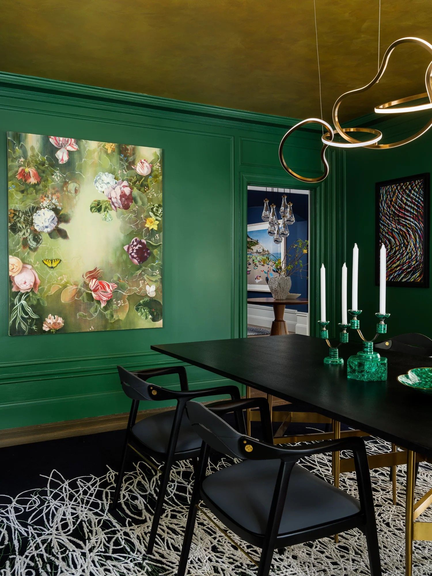 Green dining room with floral art, black table, gray chairs, and gold light fixture.