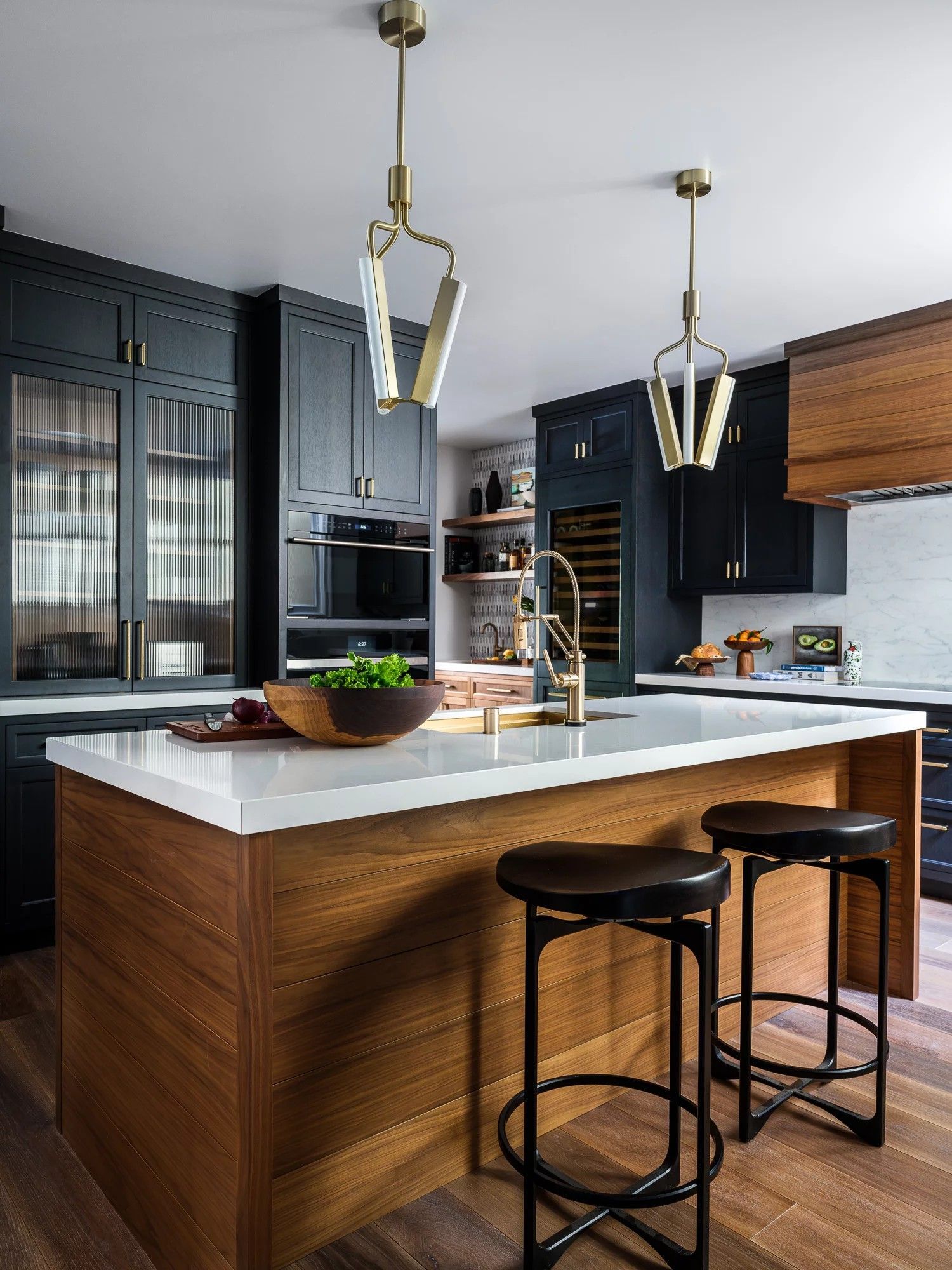 Modern kitchen with dark cabinetry, wooden island, white countertop, and gold pendant lights.