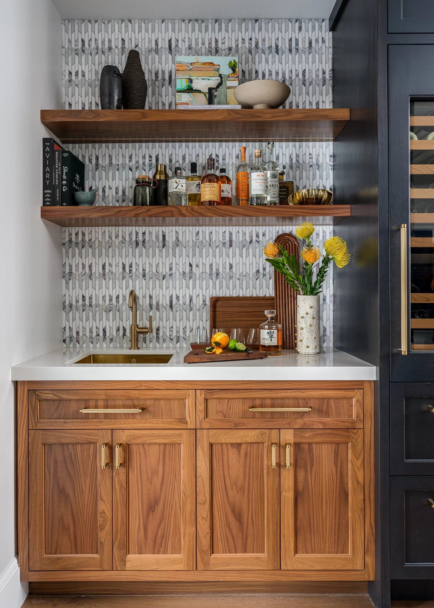 Wooden home bar with shelves, sink, and liquor bottles against patterned backsplash.