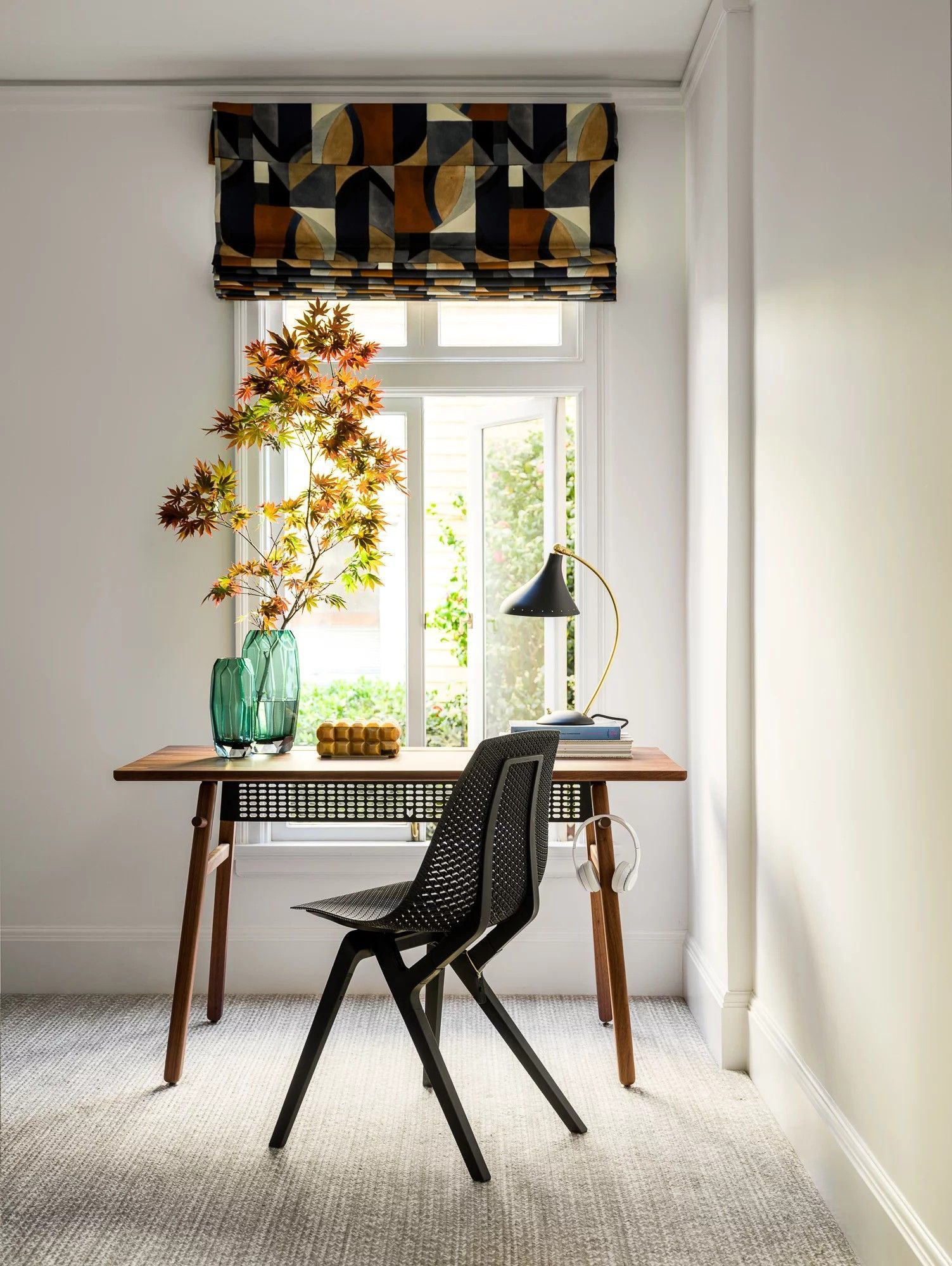 Desk area with patterned shade, black chair, and plant arrangement.