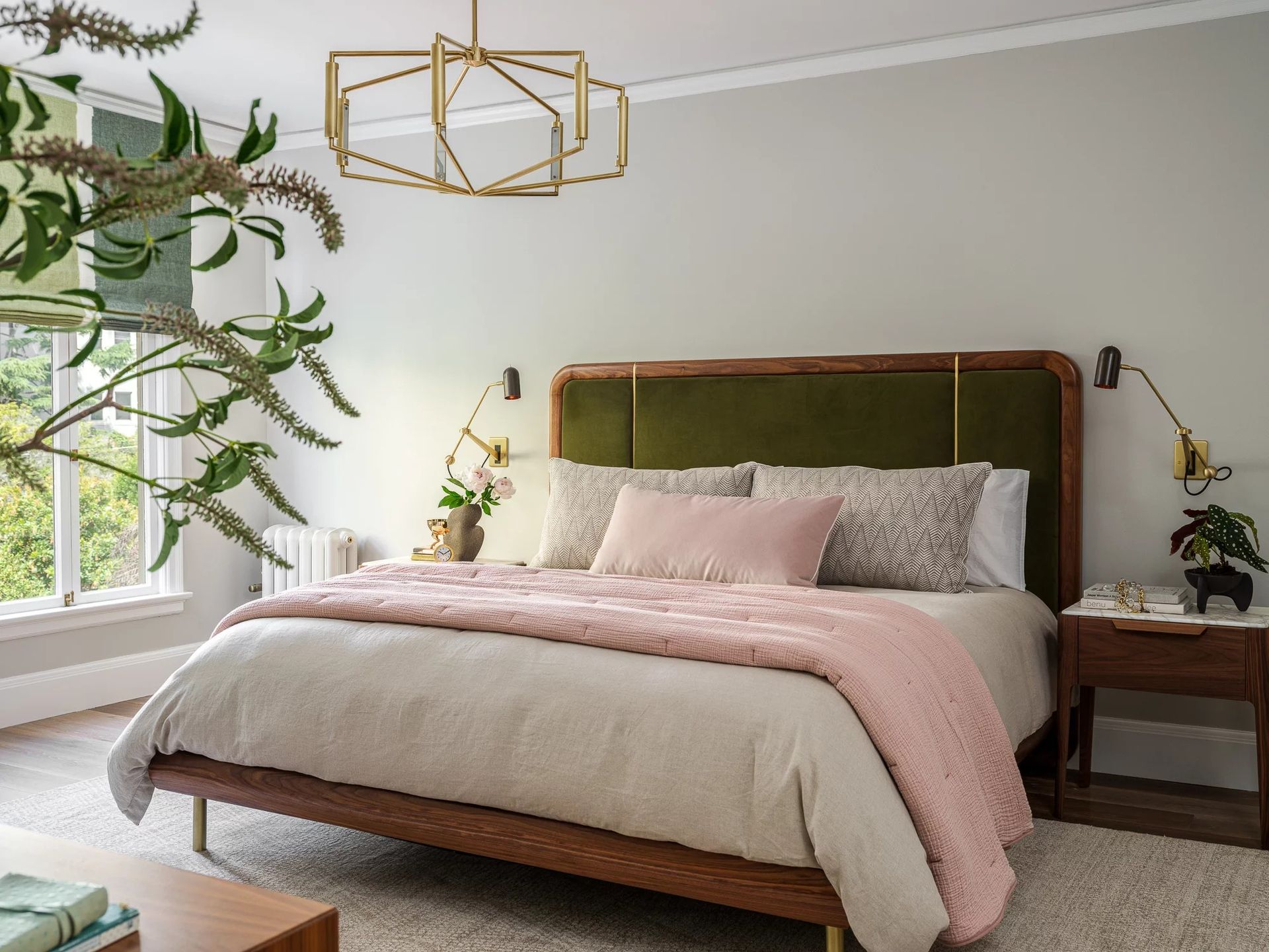 Bedroom with green headboard, pink accents, and modern gold chandelier.