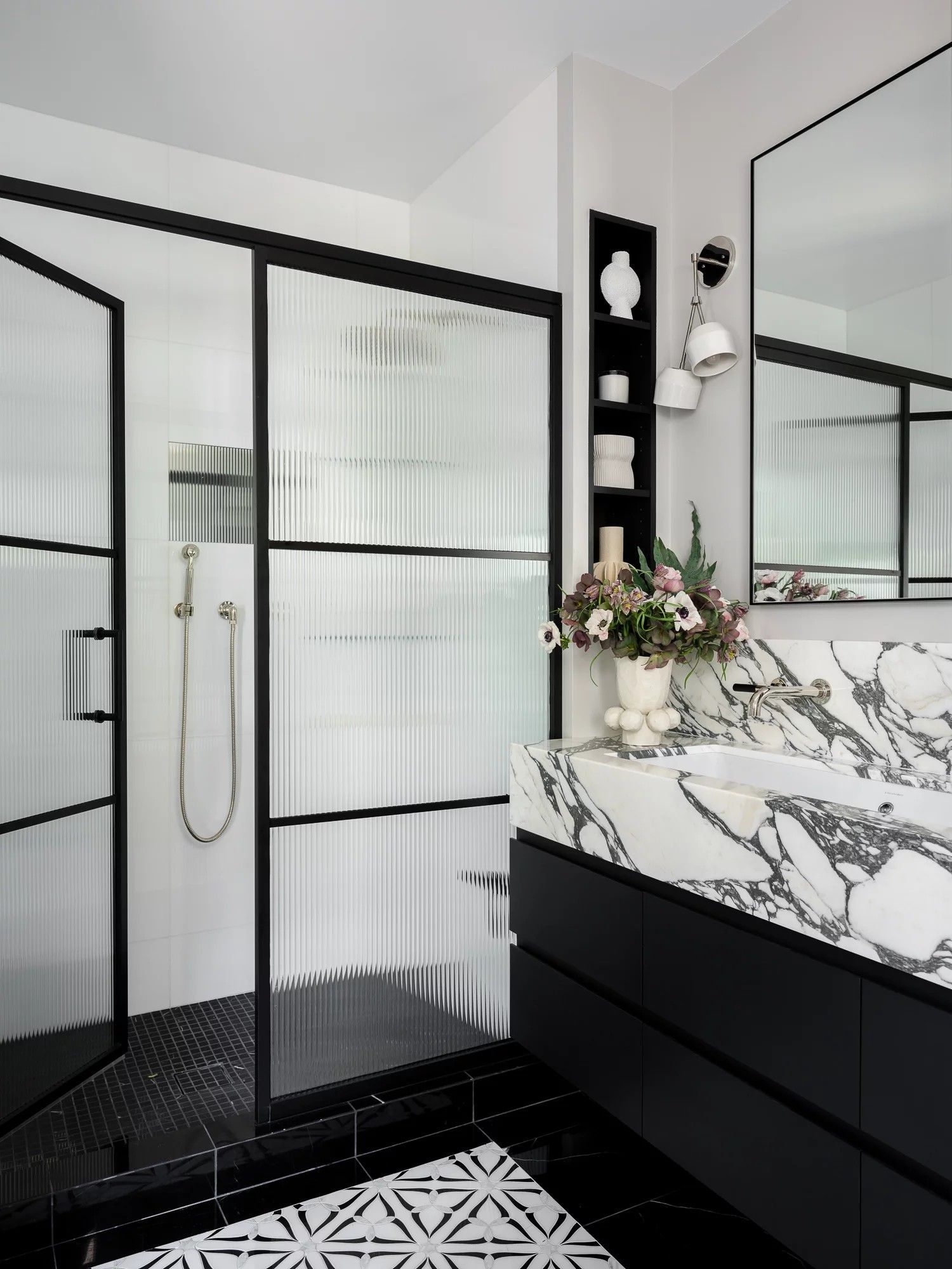 Modern black and white bathroom with marble countertop, glass shower, and patterned floor.