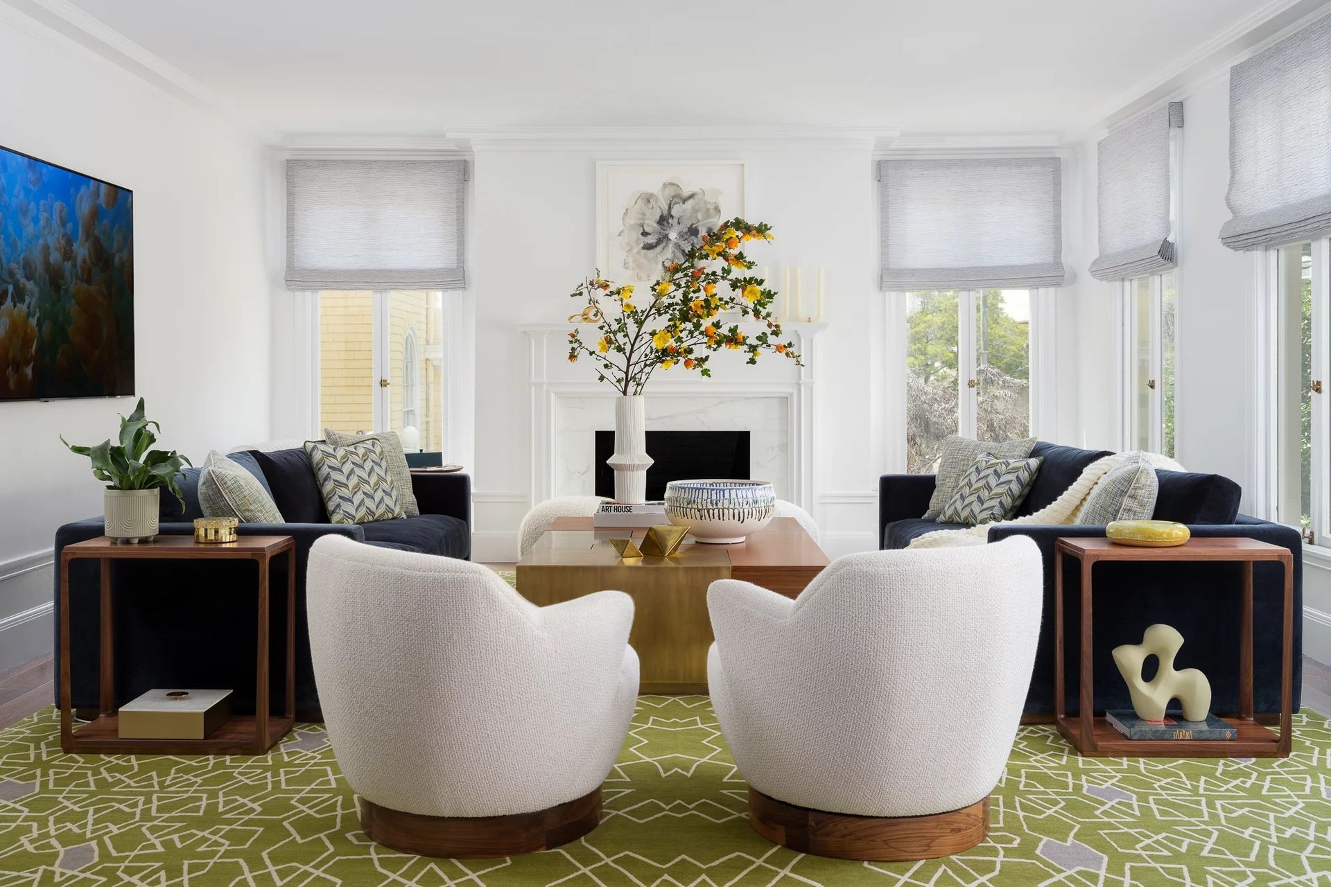 Living room with two navy sofas, white chairs, and a green patterned rug.