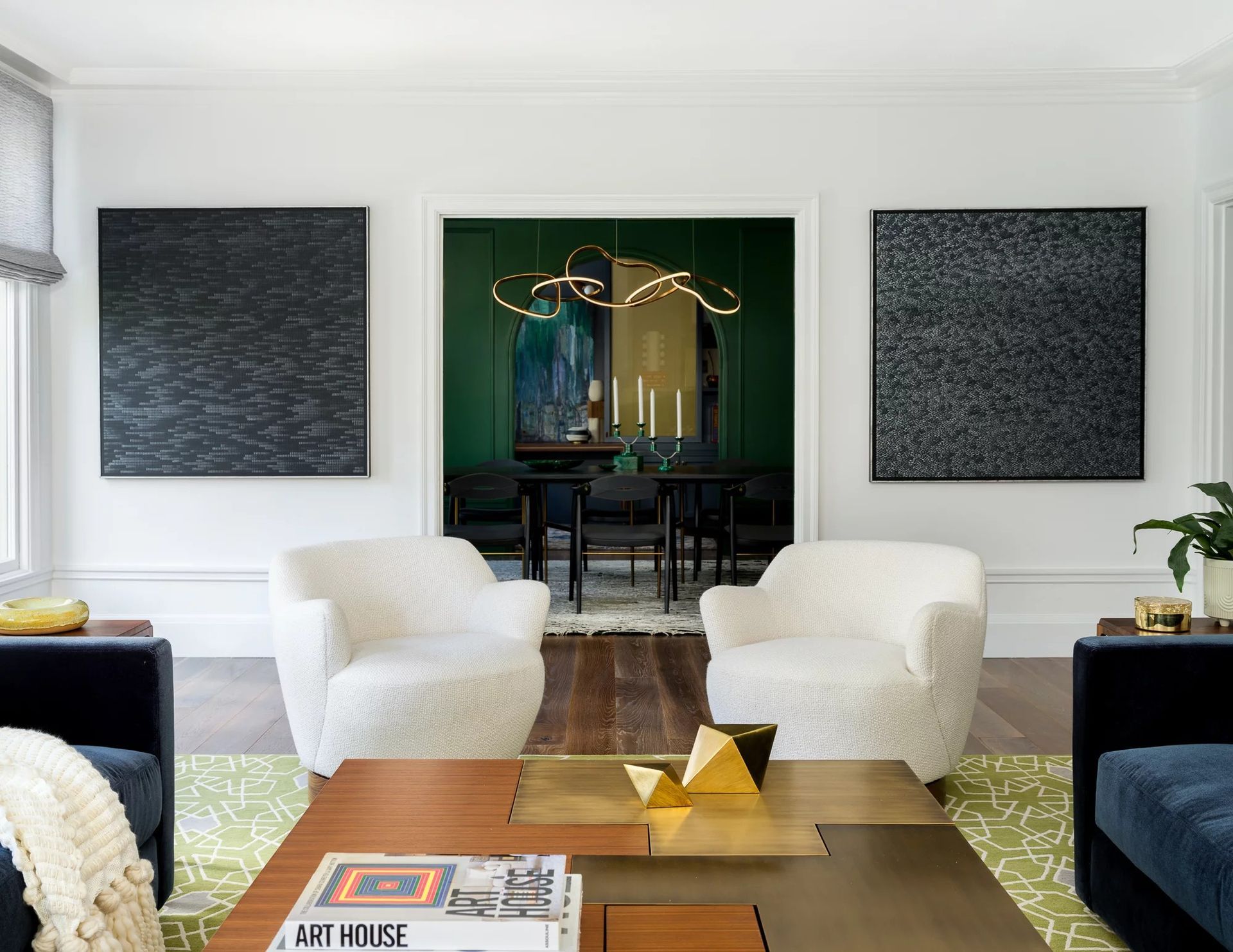 Living room with white chairs, dark artwork, and a green dining room in the background.