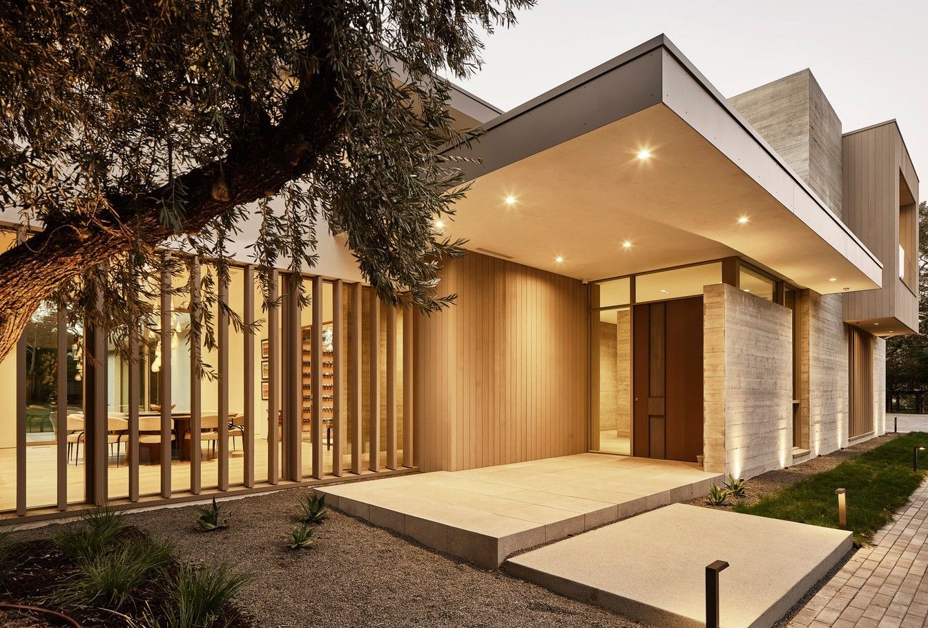 Modern house exterior with wooden facade and entrance. Stone path and landscaping.