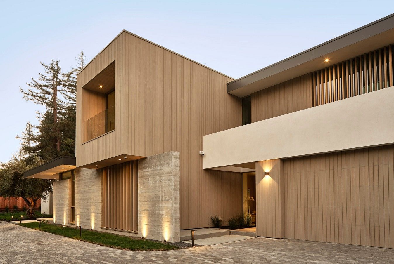 Modern home exterior with wood siding, stone accents, and inviting lighting.