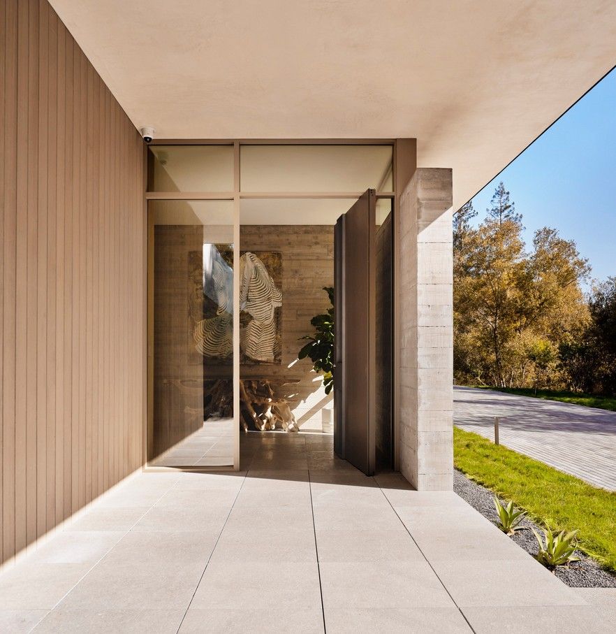 Modern home entrance with stone pathway, glass door, and wooden paneling.
