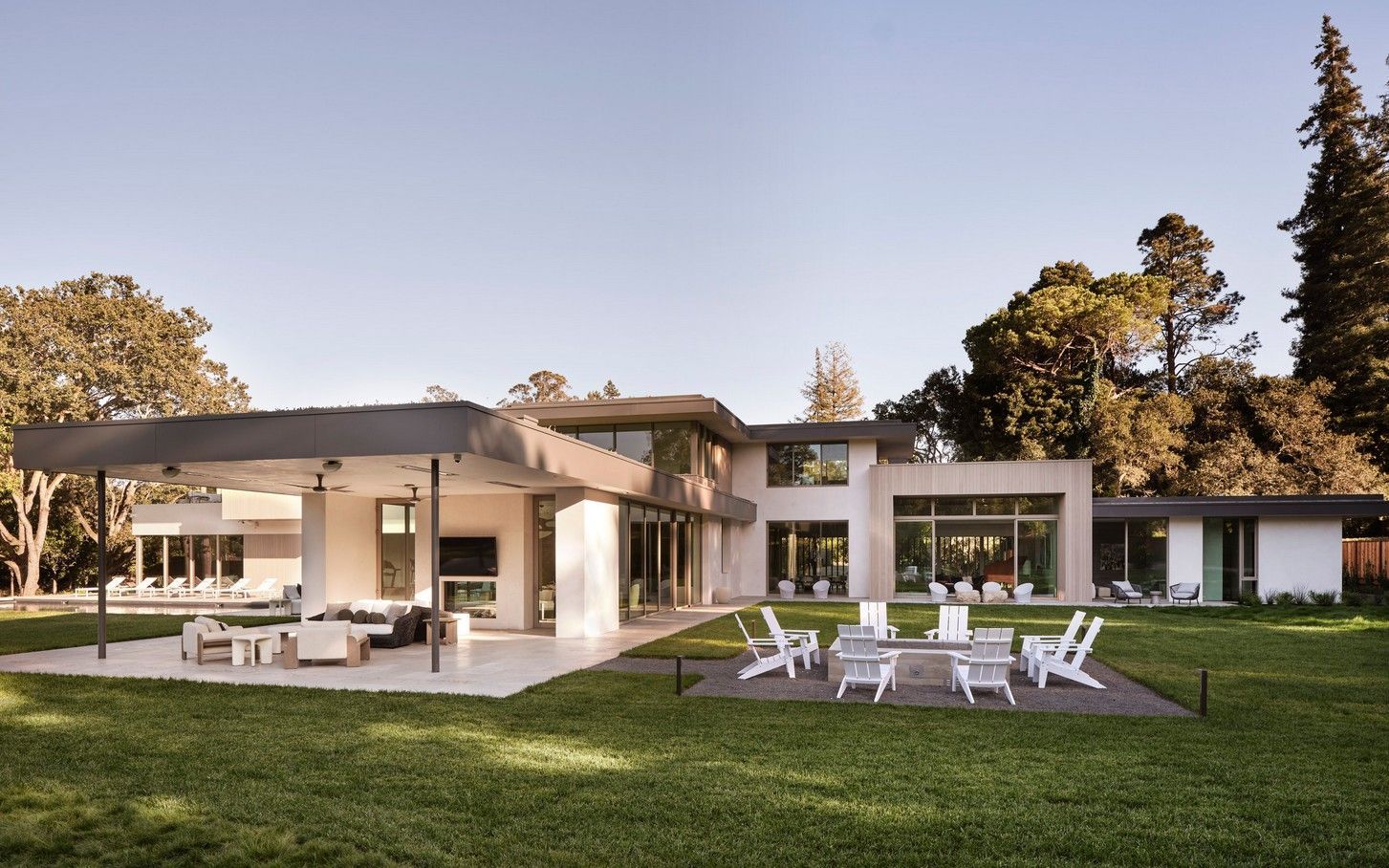 Modern two-story house with a white exterior and outdoor seating area on a grassy lawn.