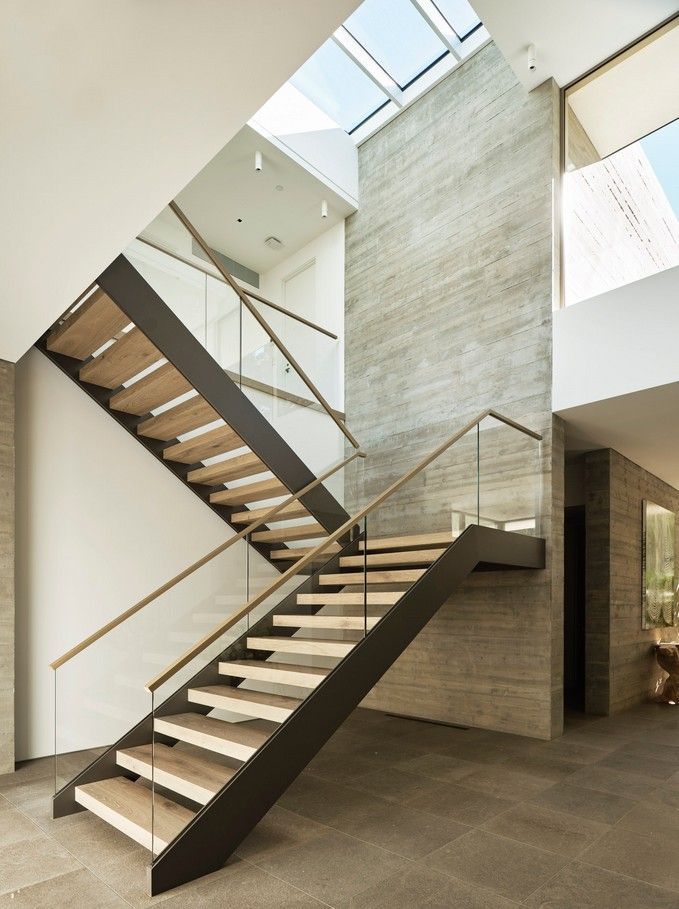 Modern interior staircase with wooden treads, metal frame, and glass railings, lit by a skylight.