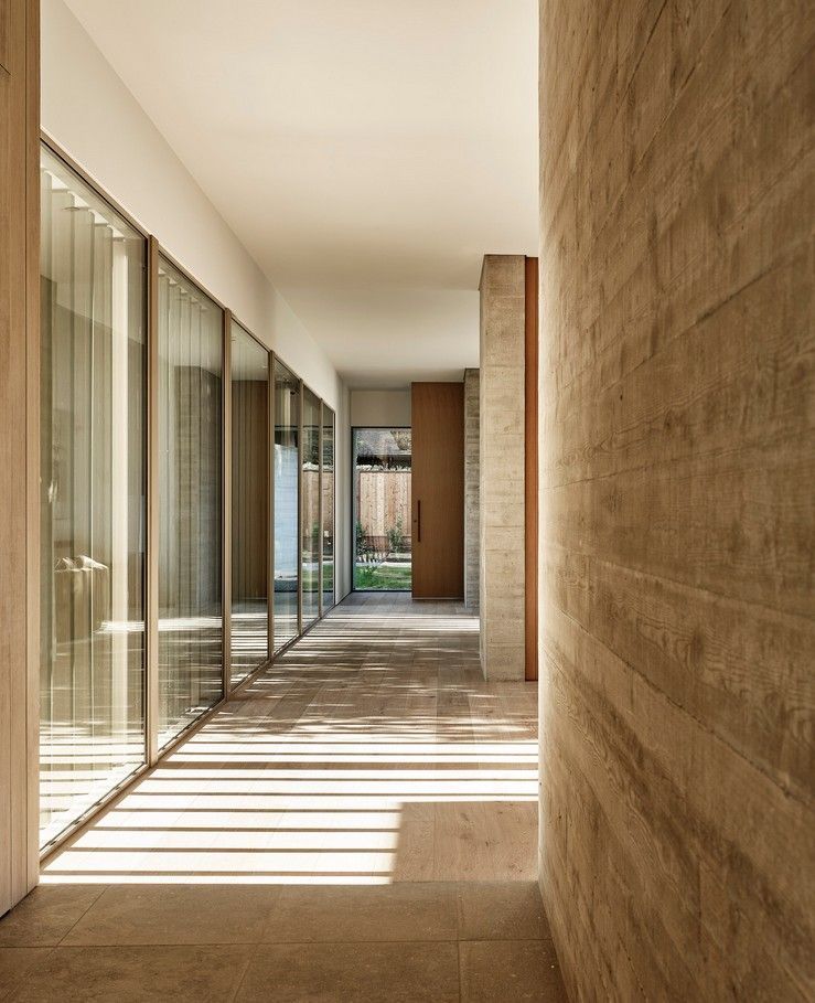 Long hallway with glass walls on the left and a textured concrete wall on the right. Sunlight streams across the floor.