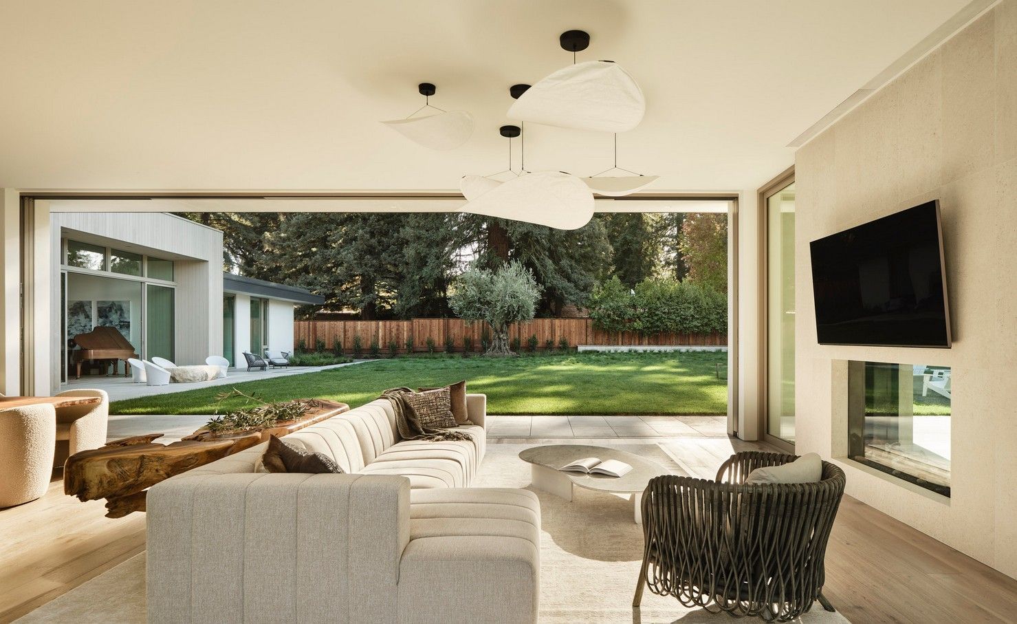 Modern living room opens to backyard. Beige sofa, neutral colors, sliding glass doors, and a green lawn.