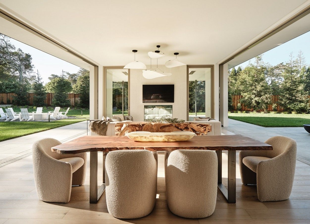 Outdoor dining area with a wooden table, textured chairs, and a view of a backyard.