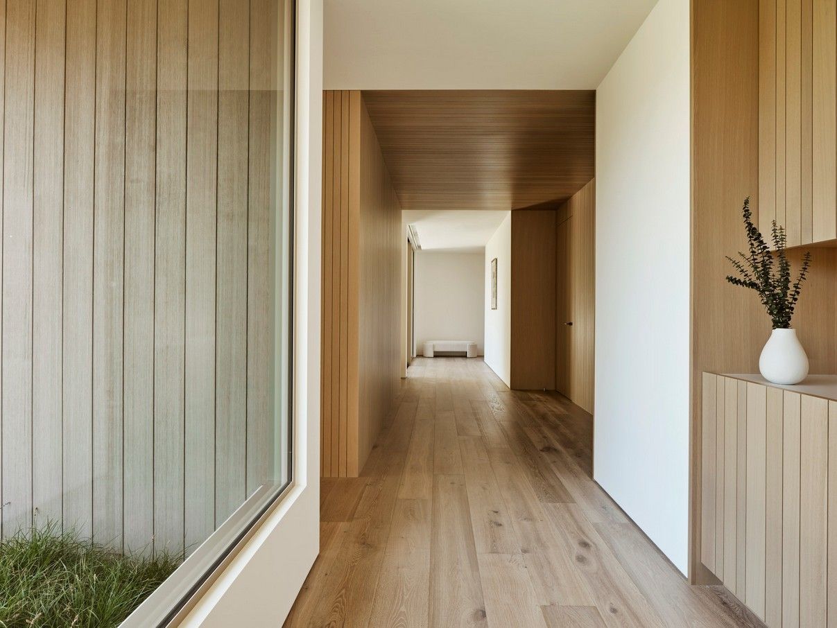 Long hallway with light wood paneling, flooring, and built-in storage. A glass wall is on the left.