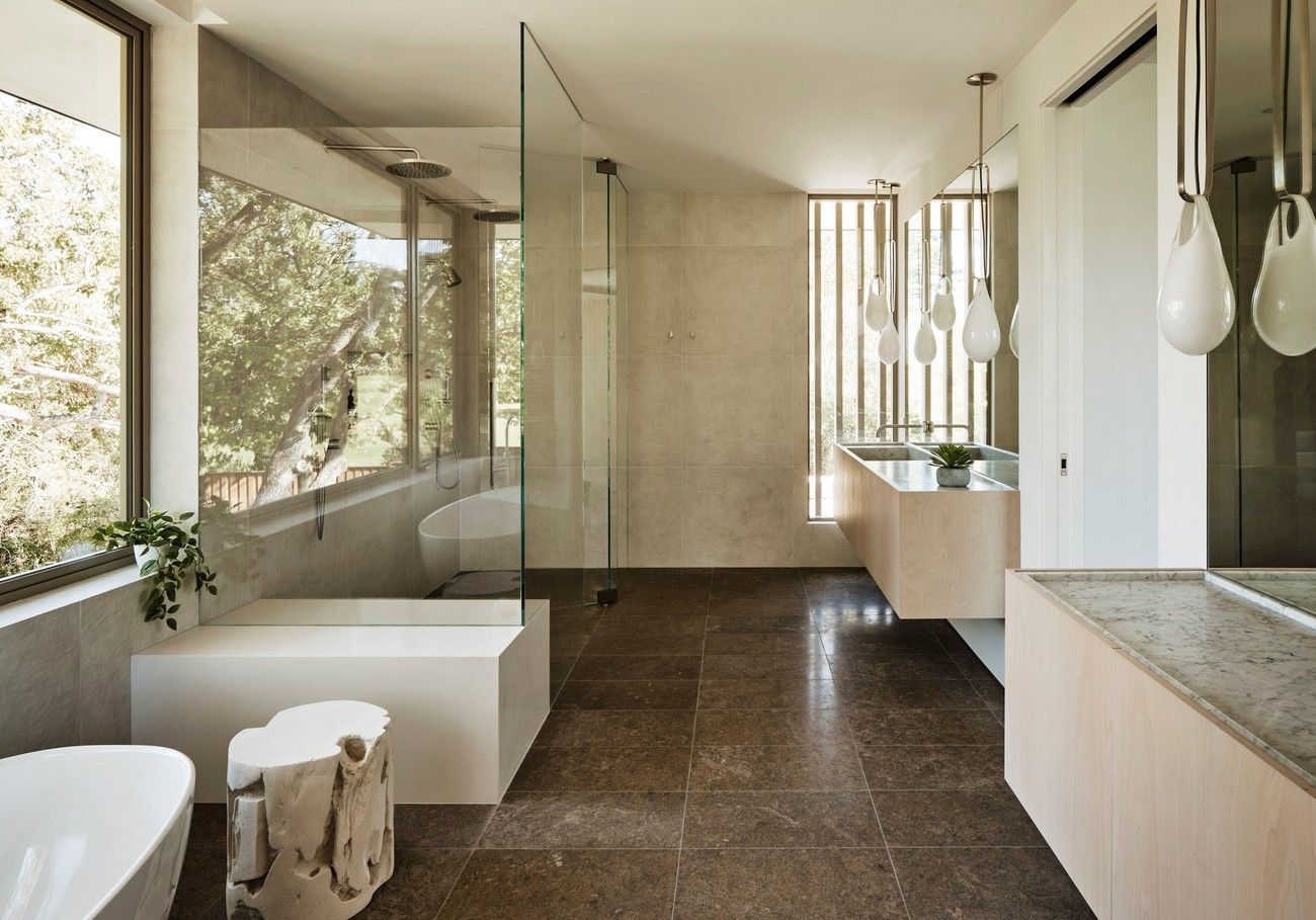 Modern bathroom with large windows, freestanding tub, glass shower, and wood vanity.