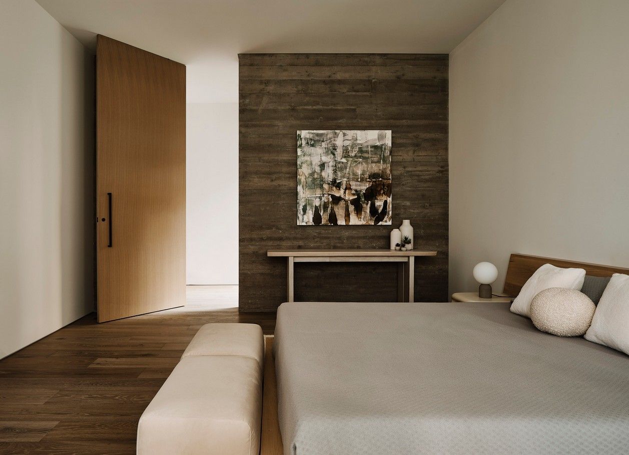 Bedroom with a large wooden door, gray bed, and artwork on a textured wall.
