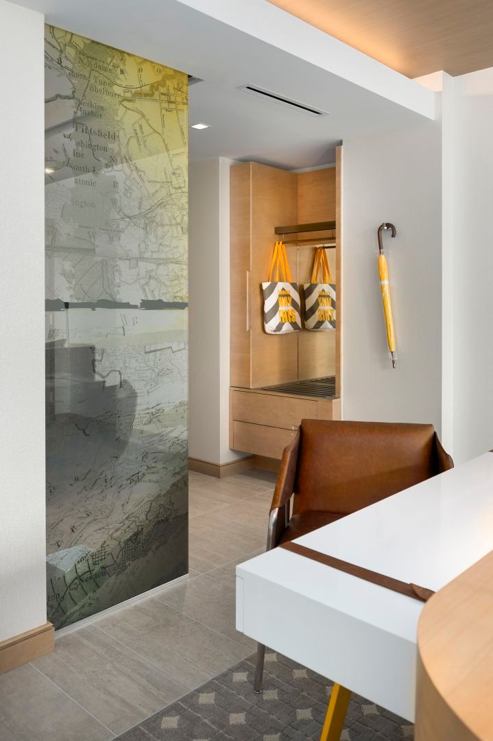 Interior with map-covered glass, closet, brown chair, and yellow umbrella. White desk in foreground.