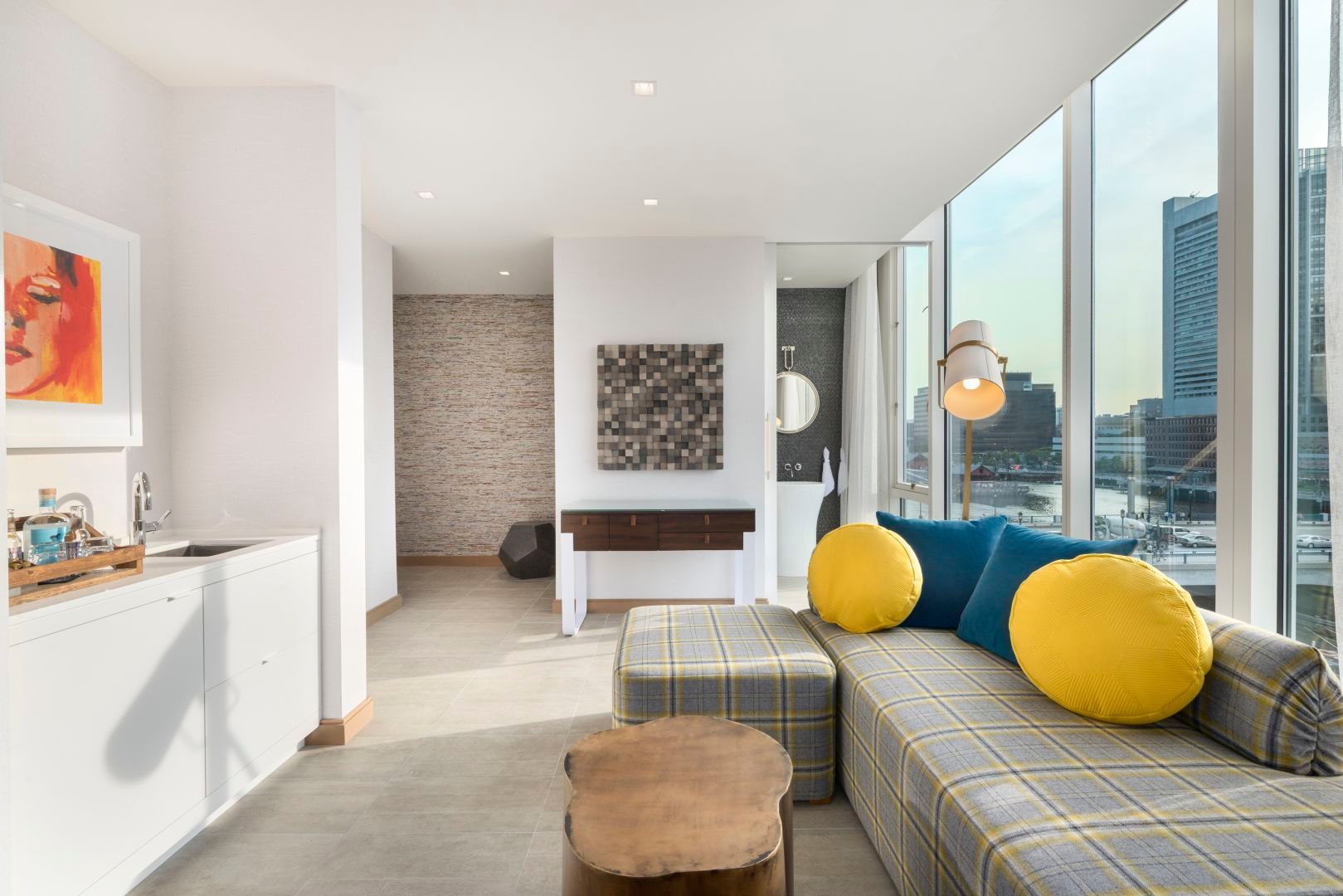 Modern living room with a window-side couch, yellow pillows, art, and city view.