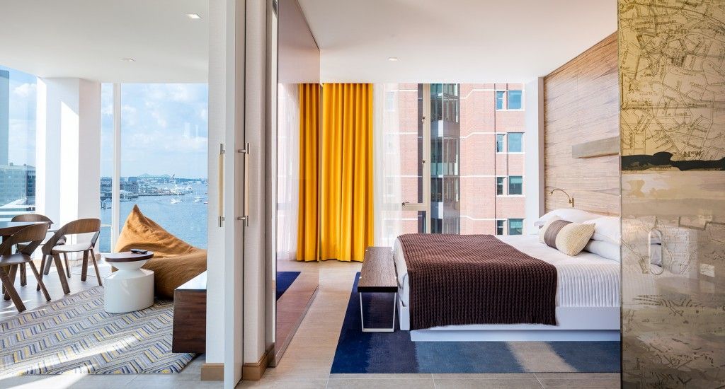 Hotel room with bed, large window overlooking water, colorful curtains and rug.
