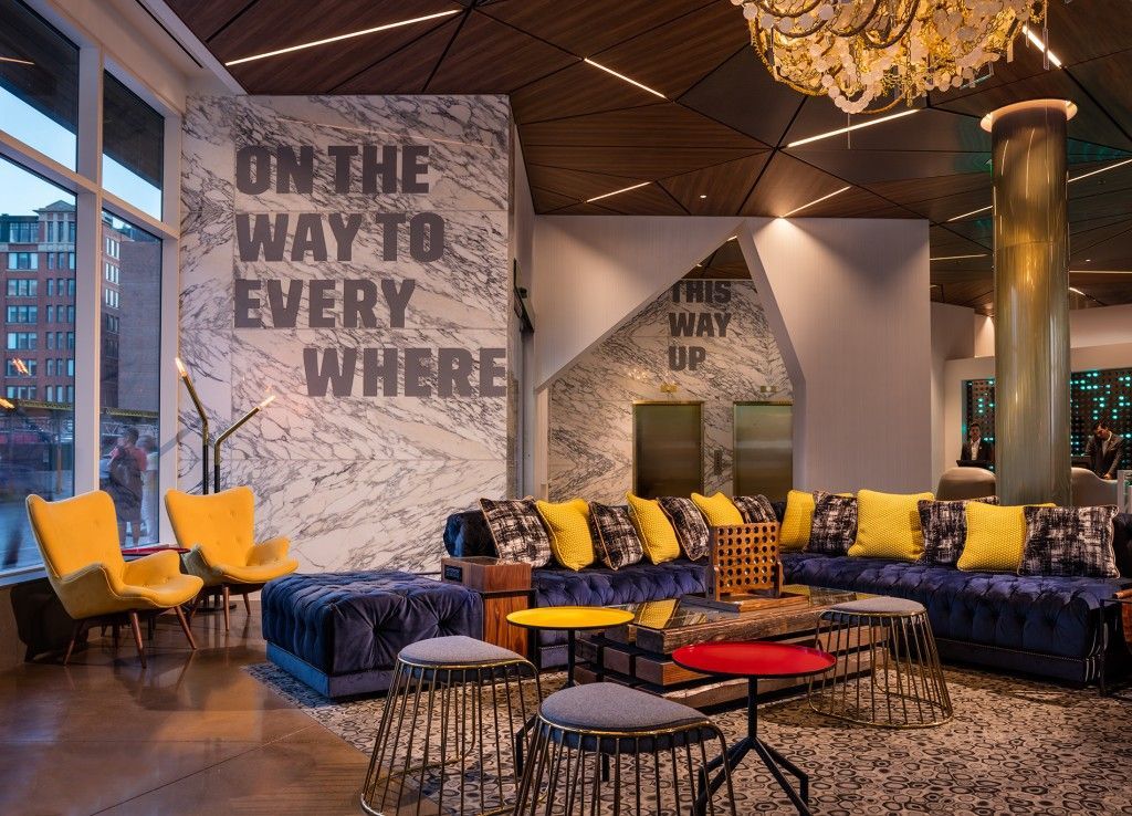 Hotel lobby with yellow chairs, blue couches, and a large wall graphic that reads 