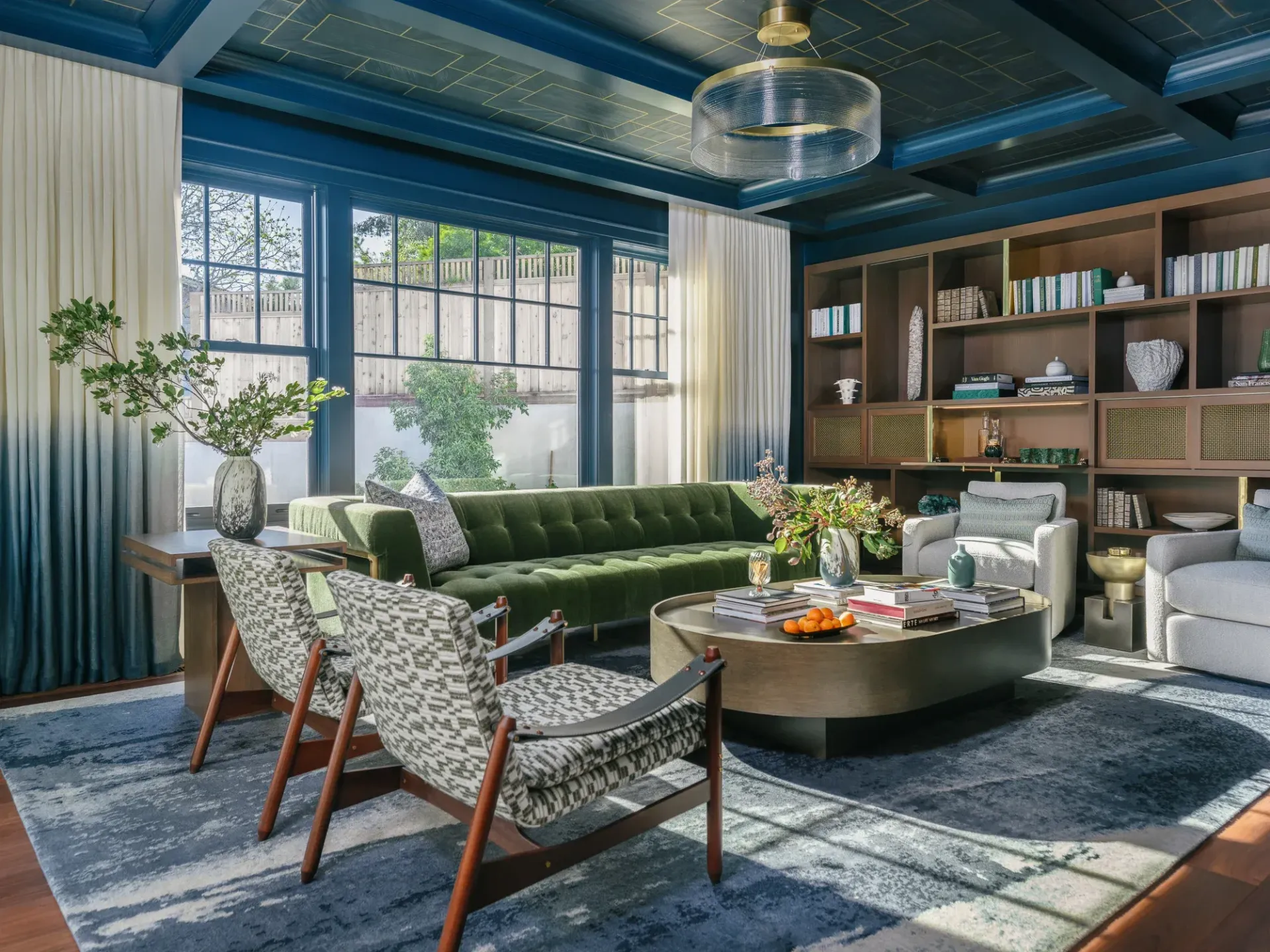Living room with green velvet sofa, armchairs, built-in bookshelves, and blue ombre curtains.