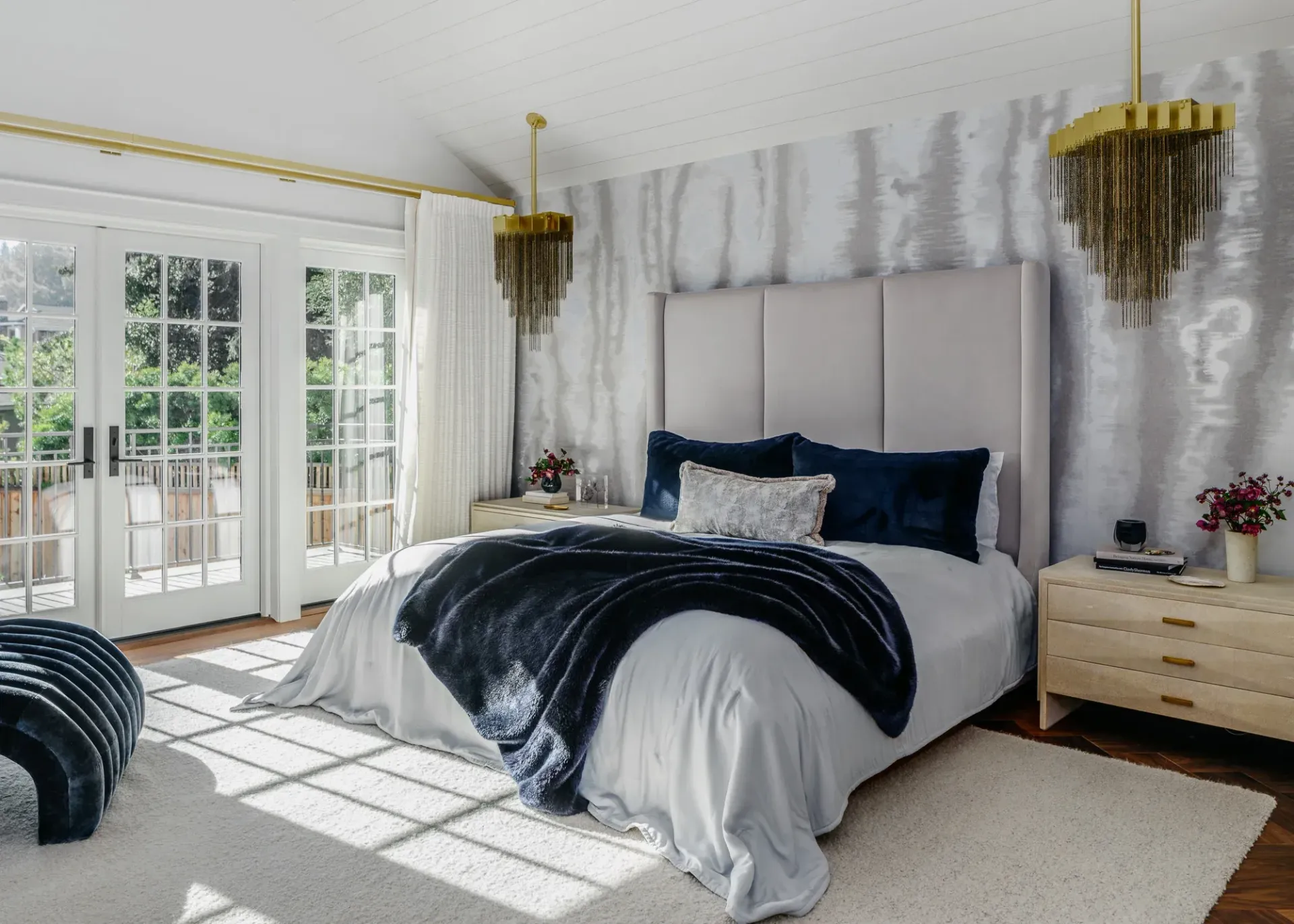 Bedroom with bed, French doors, and patterned wallpaper. Gold accents and blue and white bedding.