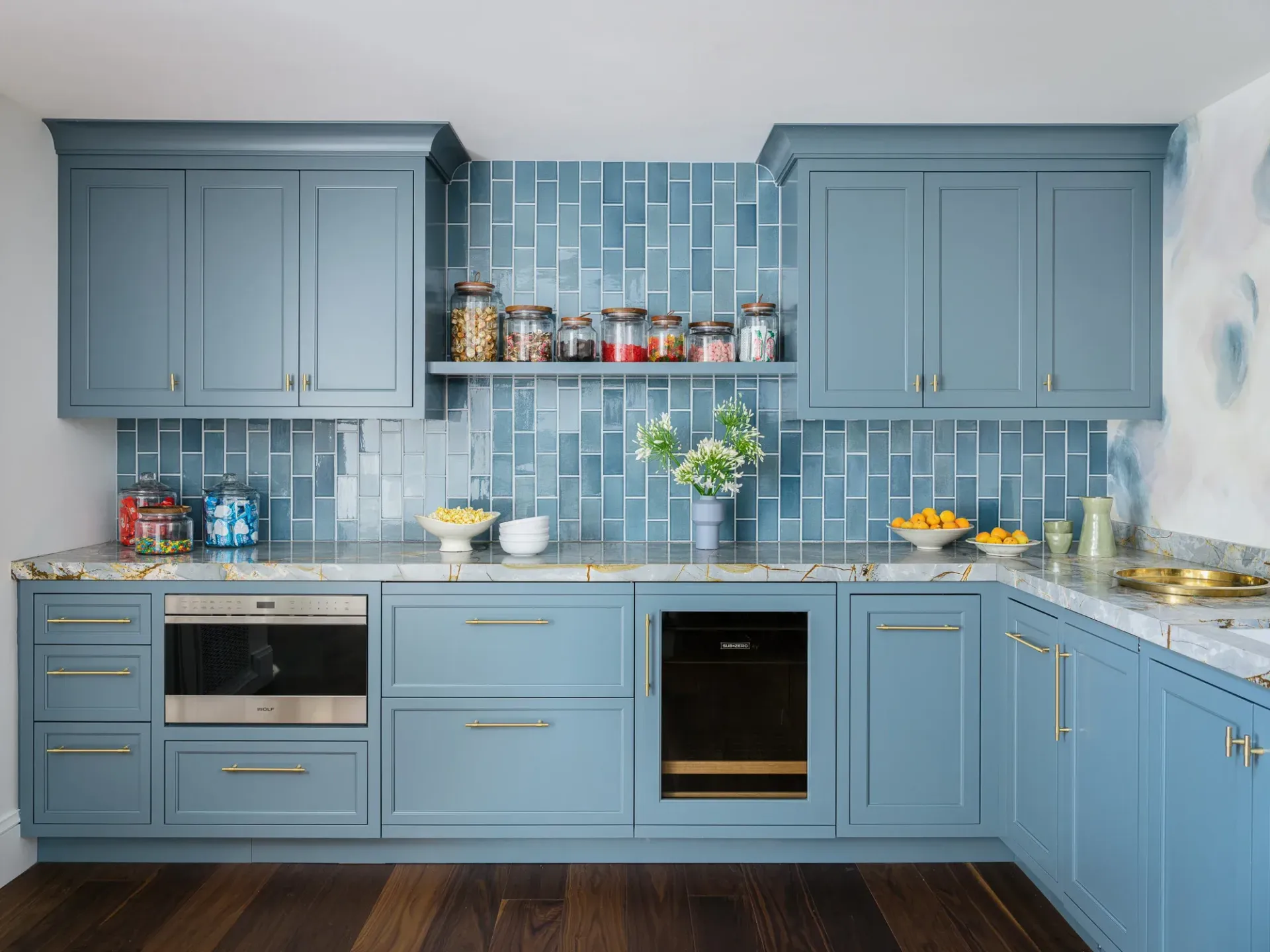 Blue kitchen with matching cabinets, a tiled backsplash, and dark wooden floors.