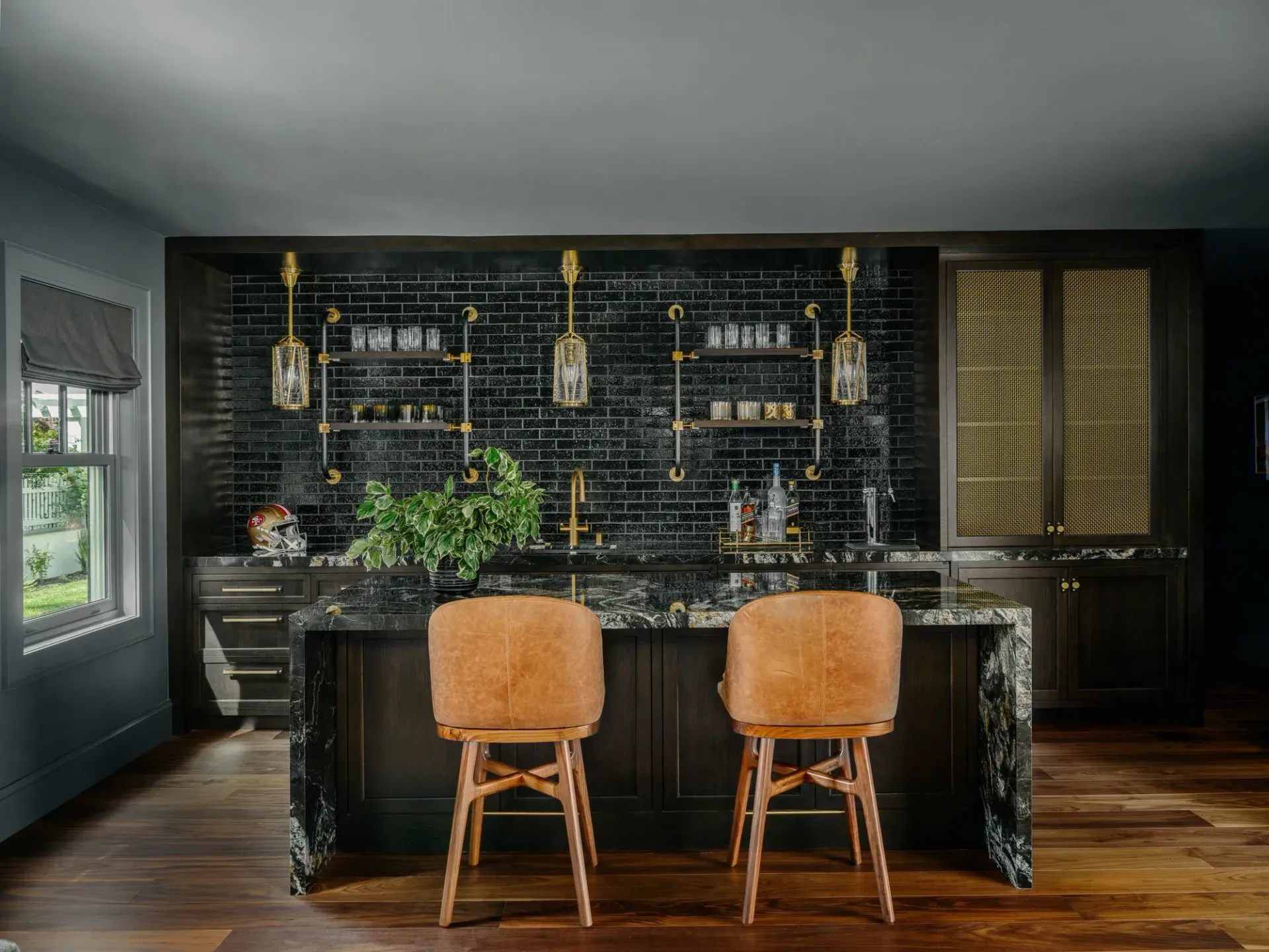 A home bar with black tile, gold accents, and leather bar stools.