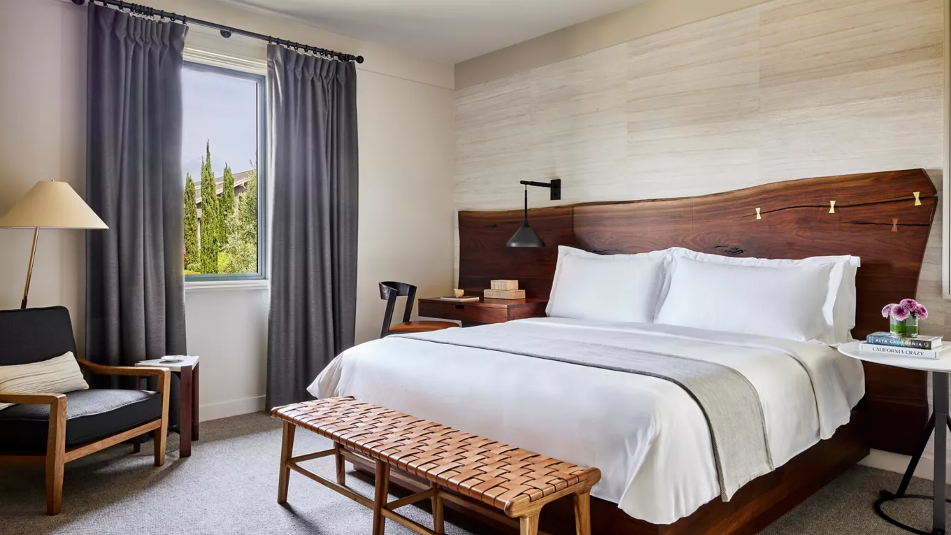 Bedroom with a large bed, wooden headboard, window with gray curtains, armchair, and side table.