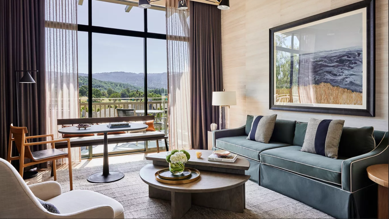 Living room with large window overlooking a scenic view, gray sofa, coffee table, and beige rug.