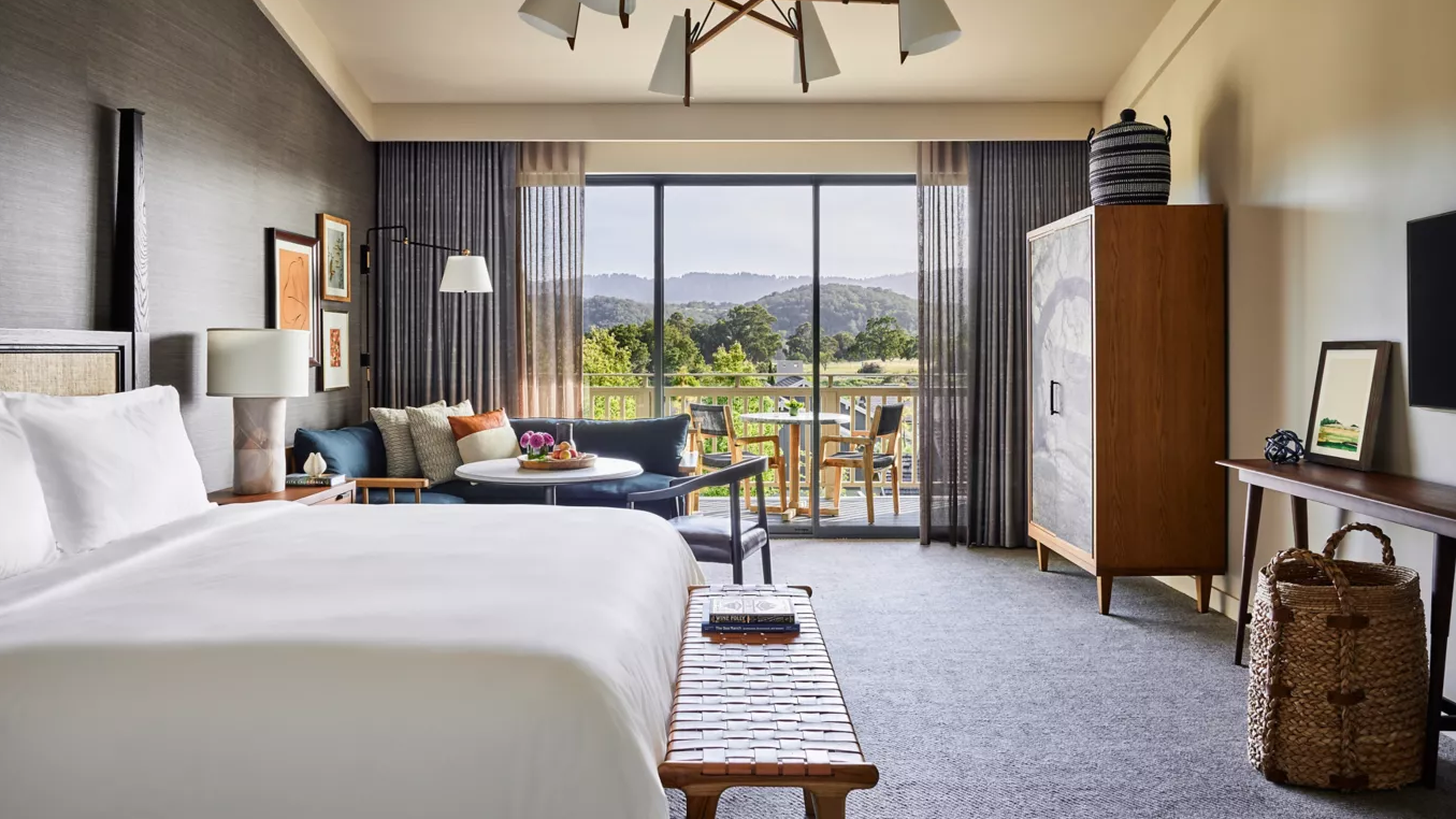 Hotel room with a large bed, seating area, and balcony overlooking a scenic landscape.