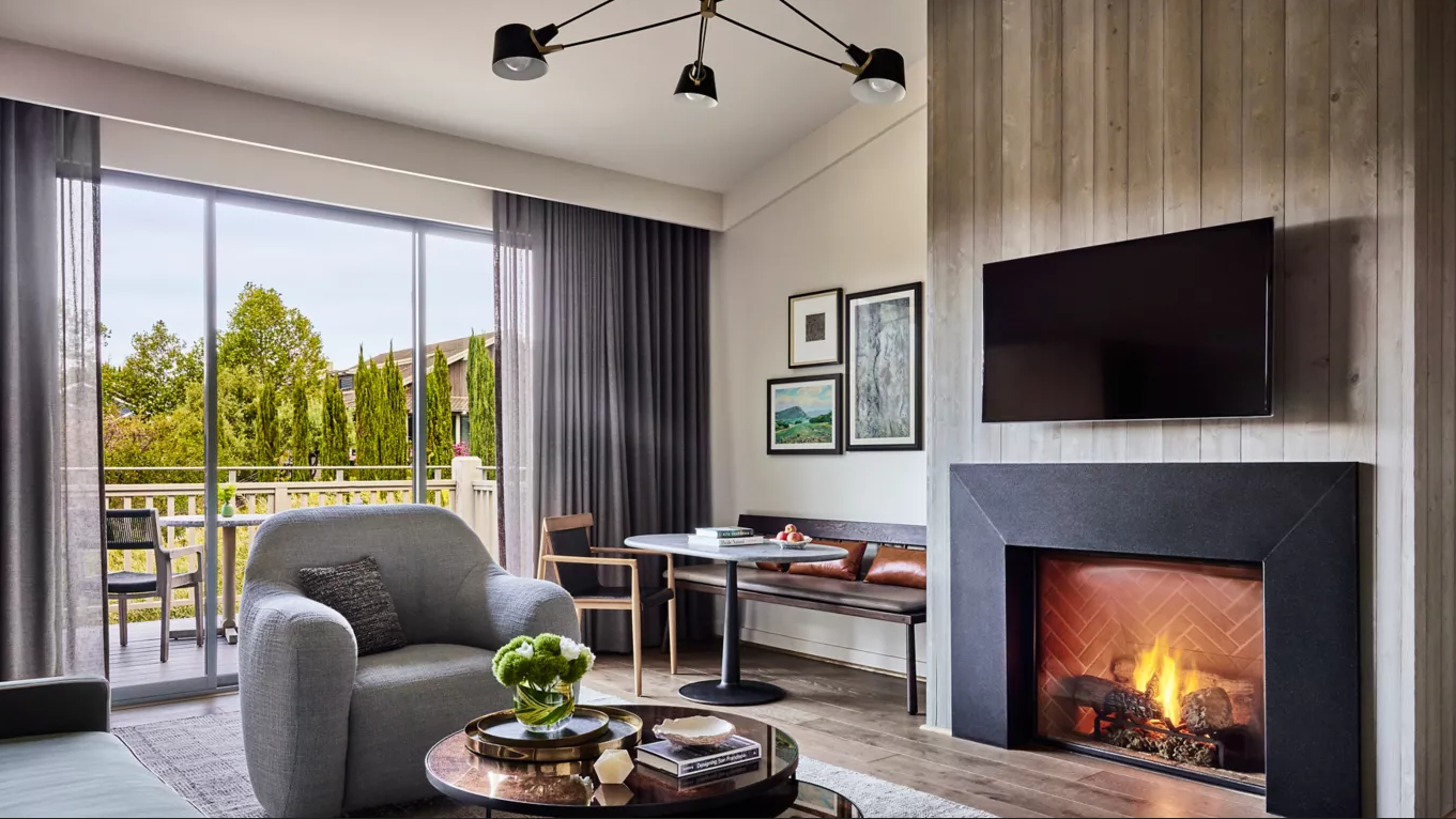 Cozy living room with fireplace, armchair, and balcony access.  Gray tones, neutral wooden accents, and an overhead light.