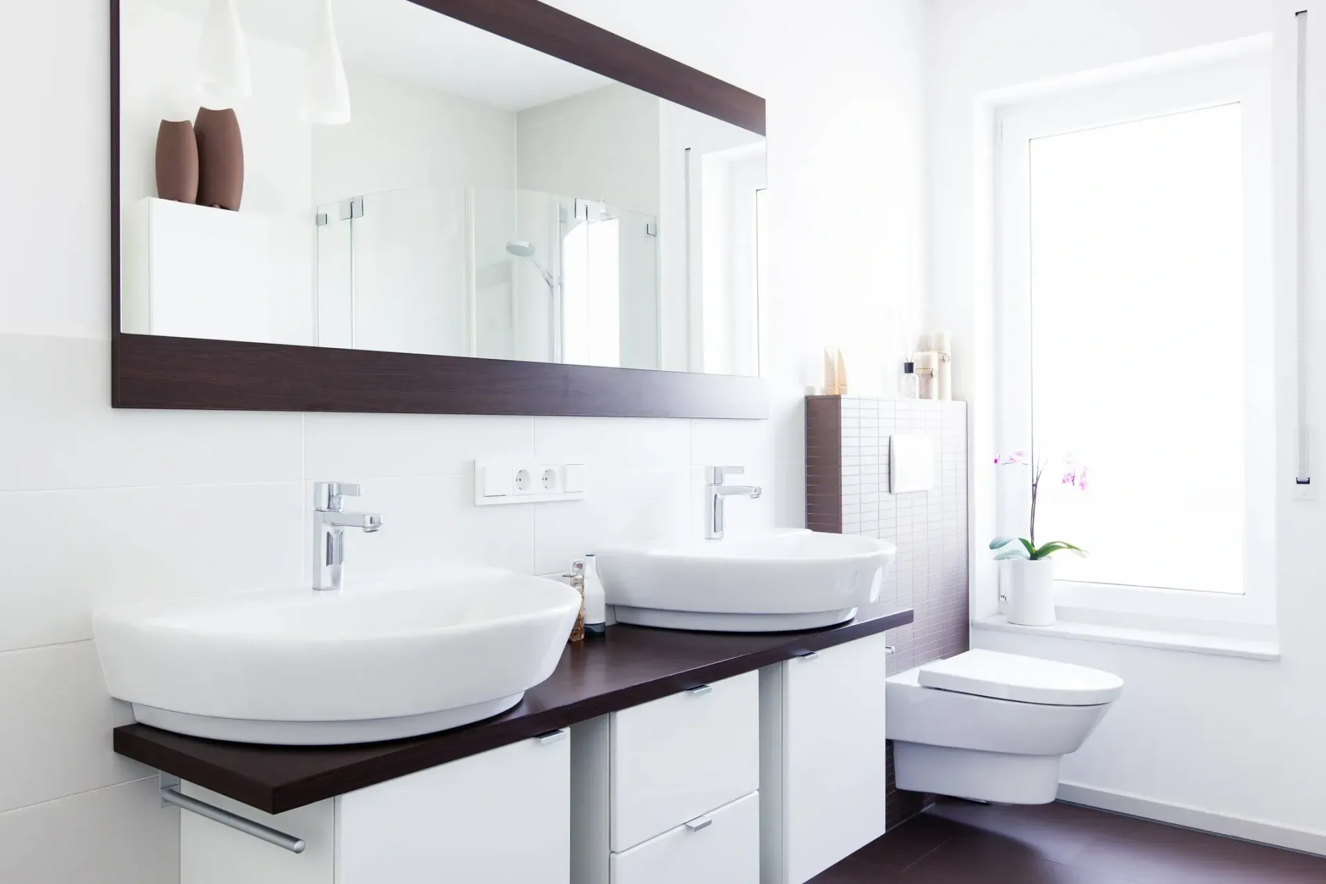 Modern white bathroom with double sinks, large mirror, and toilet.