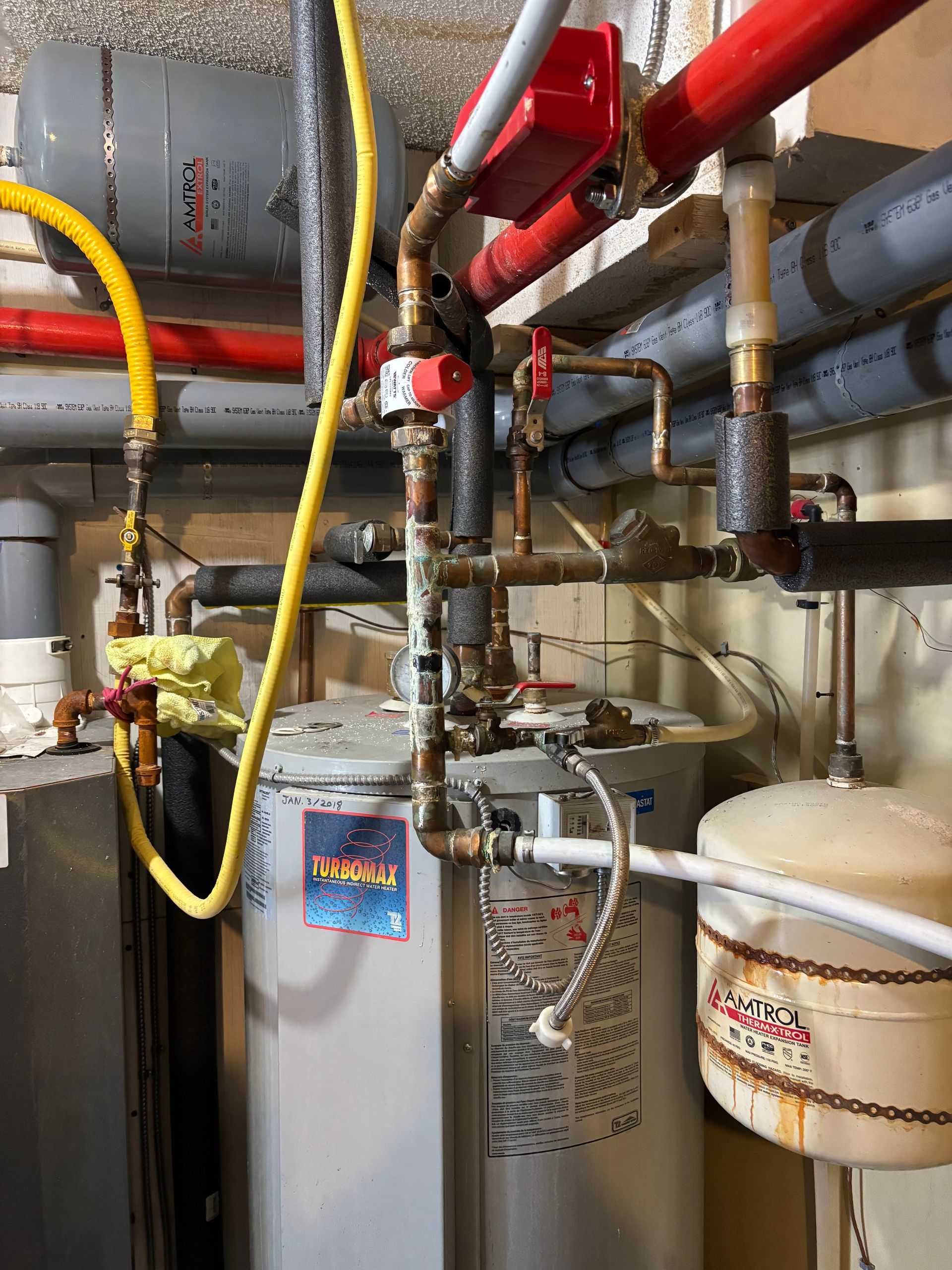 Plumbing system: a hot water heater with connected pipes, valves, and a small expansion tank, located in a basement.