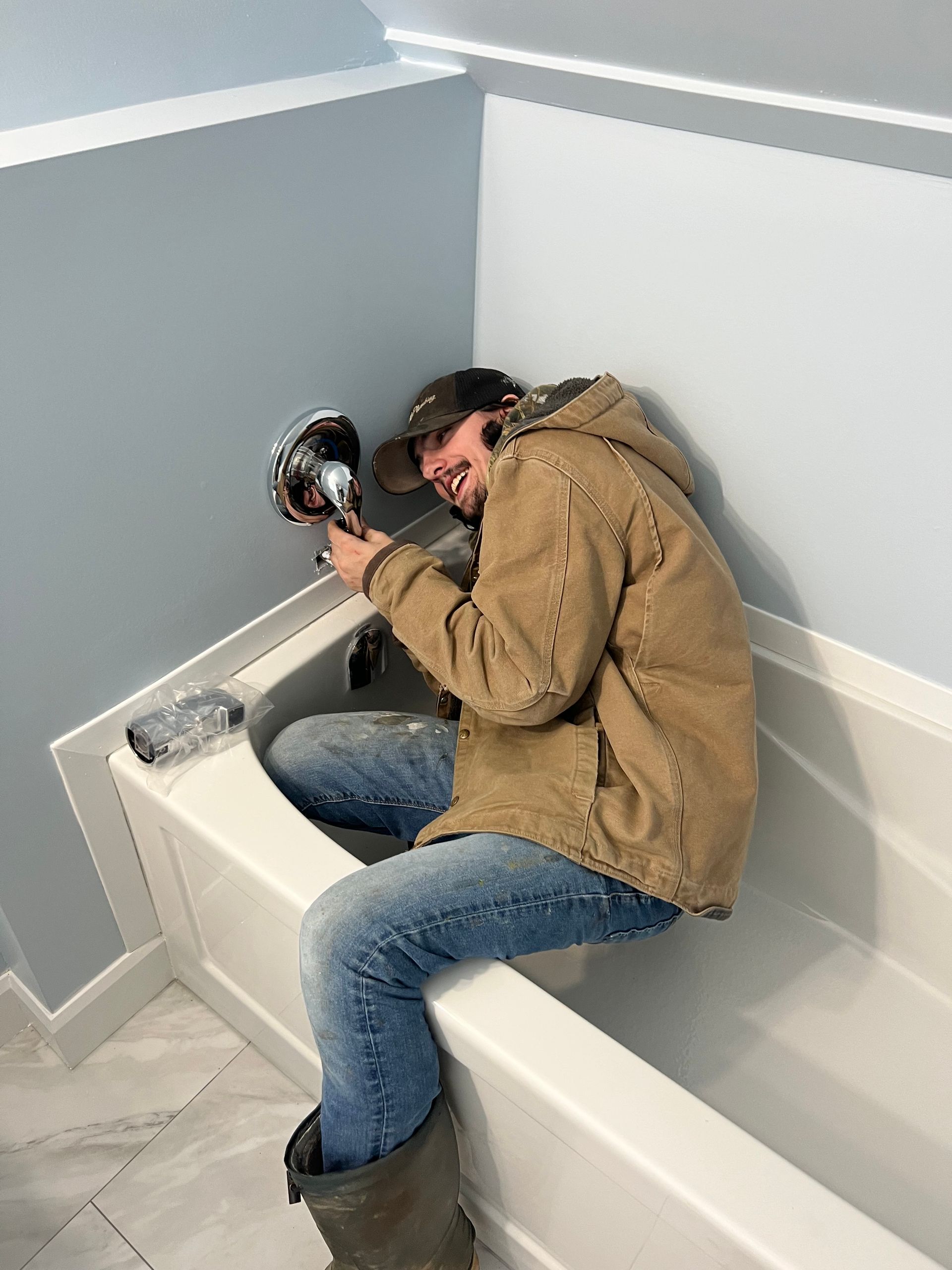 Person in work clothes holding a light inside a white bathtub; blue walls.