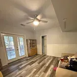 Empty living room with wood-look flooring, ceiling fan, French doors, and a couch in the corner