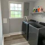 Laundry room with gray washer and dryer, window, and shelf of cleaning supplies