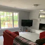 Bright living room with red sofa, wall-mounted TV, fireplace, and large window overlooking greenery