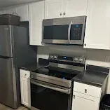 Modern kitchen with stainless steel refrigerator, microwave, and stove, framed by white cabinets and dark countertops