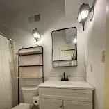 Small bathroom vanity with mirror, wall sconces, towel shelf, and white cabinetry